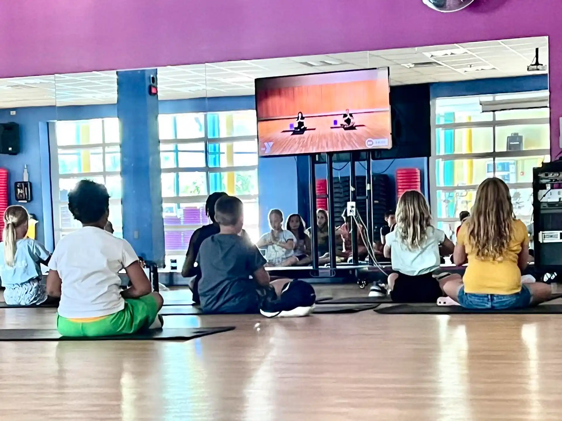 a group of people sitting on the floor in a room with a large screen