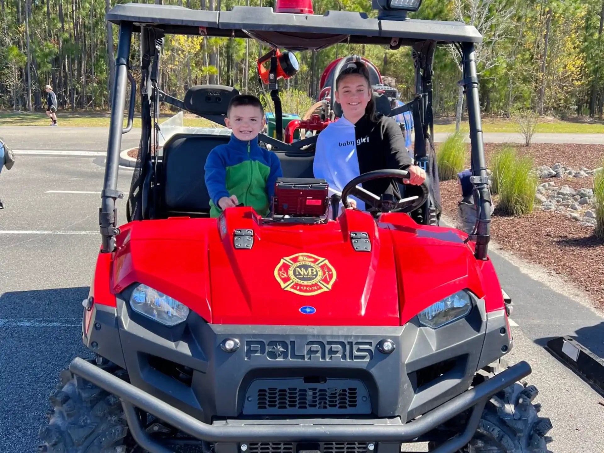 a couple of kids in a red vehicle with trees in the background