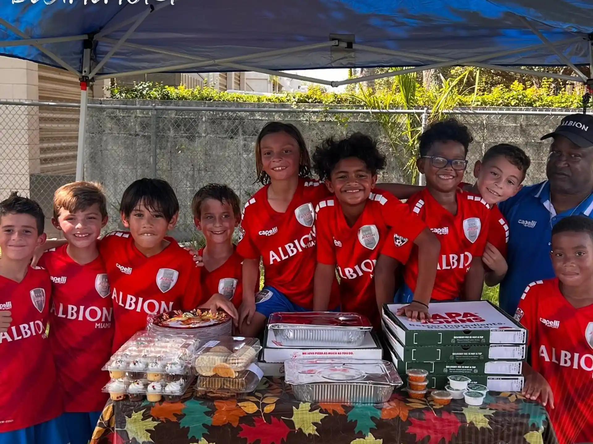 a group of people wearing matching red shirts standing next to a table with food on it