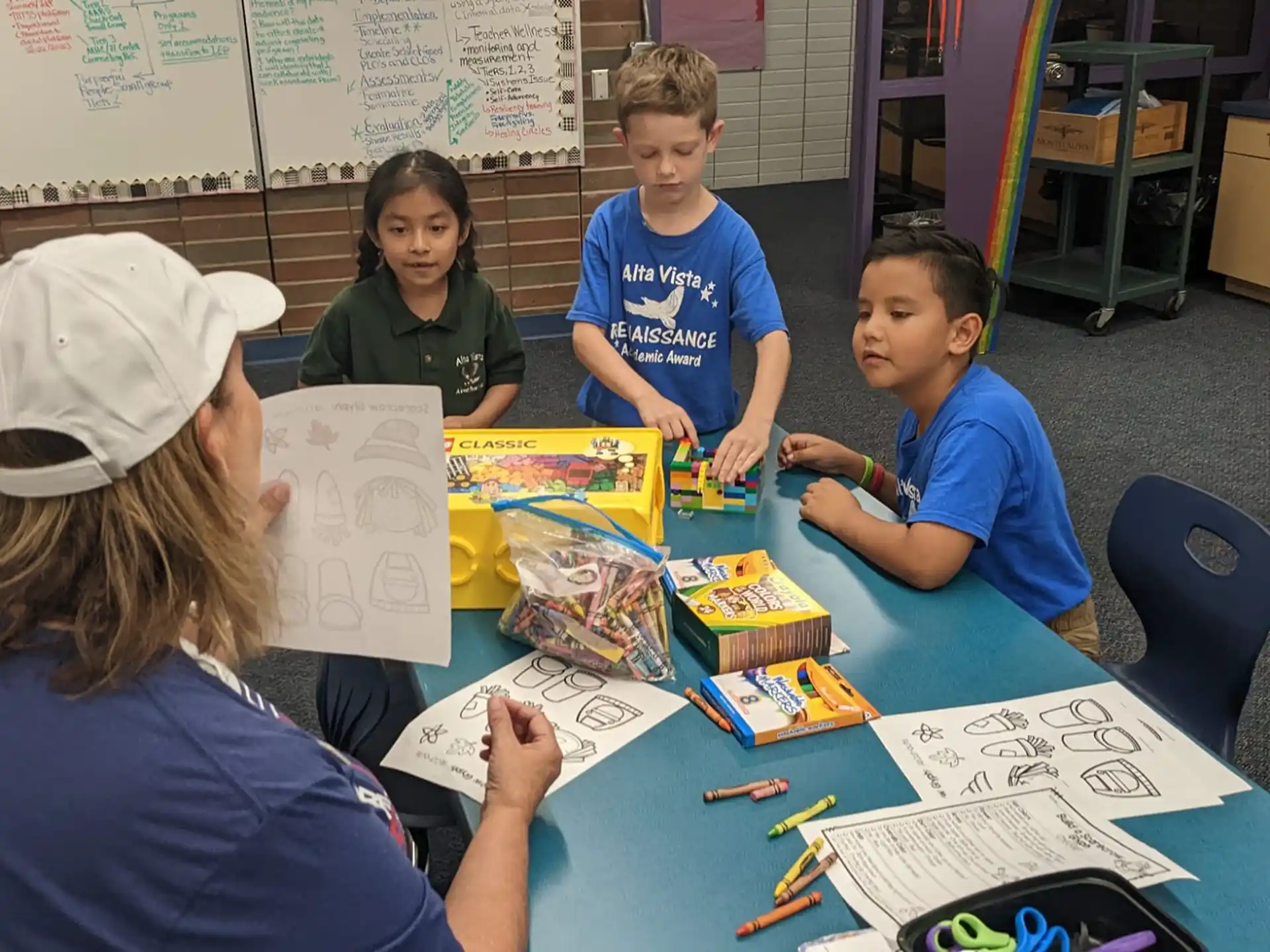 a group of children sitting at a table with a person standing behind them