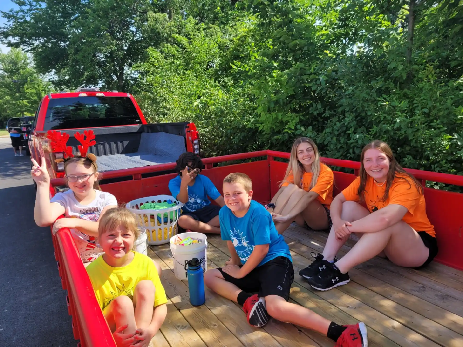 a group of kids sitting on a deck with a red truck and trees