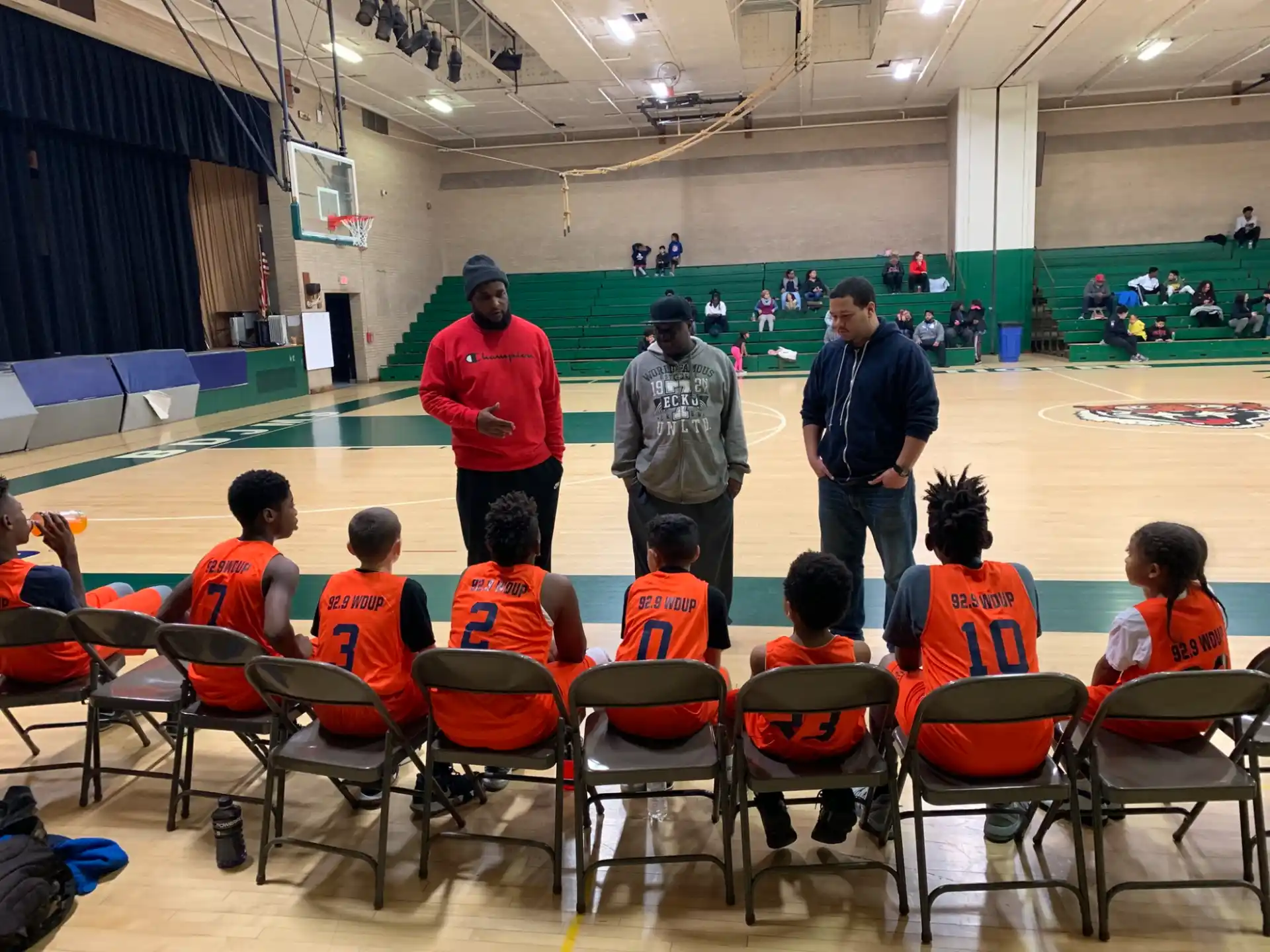 a group of people in orange vests in a room with a green wall and a person standing