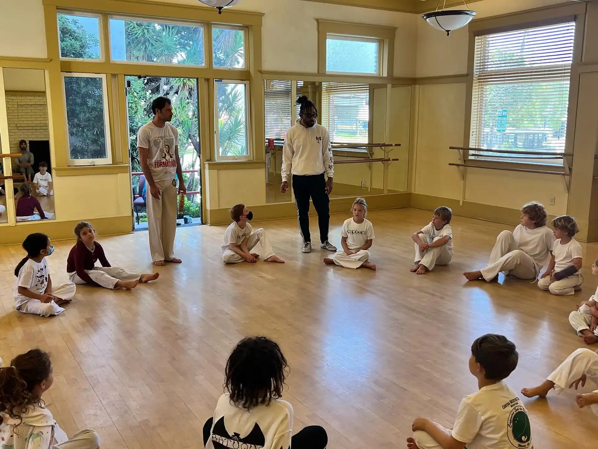 a group of people sitting in a room with a person standing on a wood floor