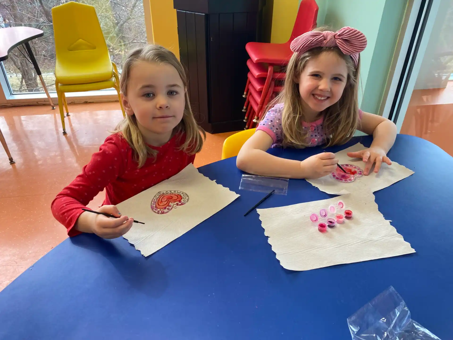 a couple of girls sitting at a table with paper and pencils