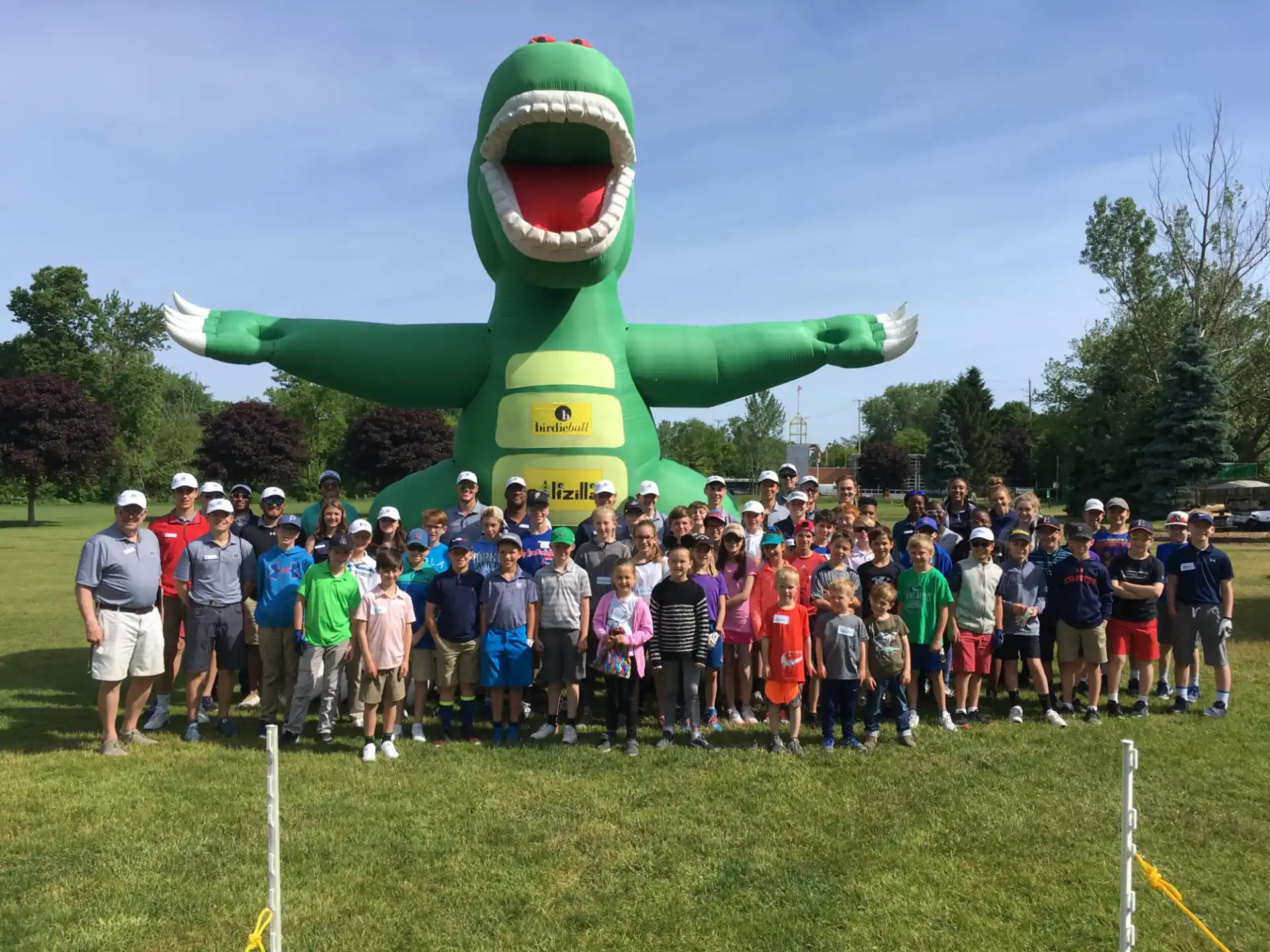 a group of people posing for a photo in front of a large green dinosaur