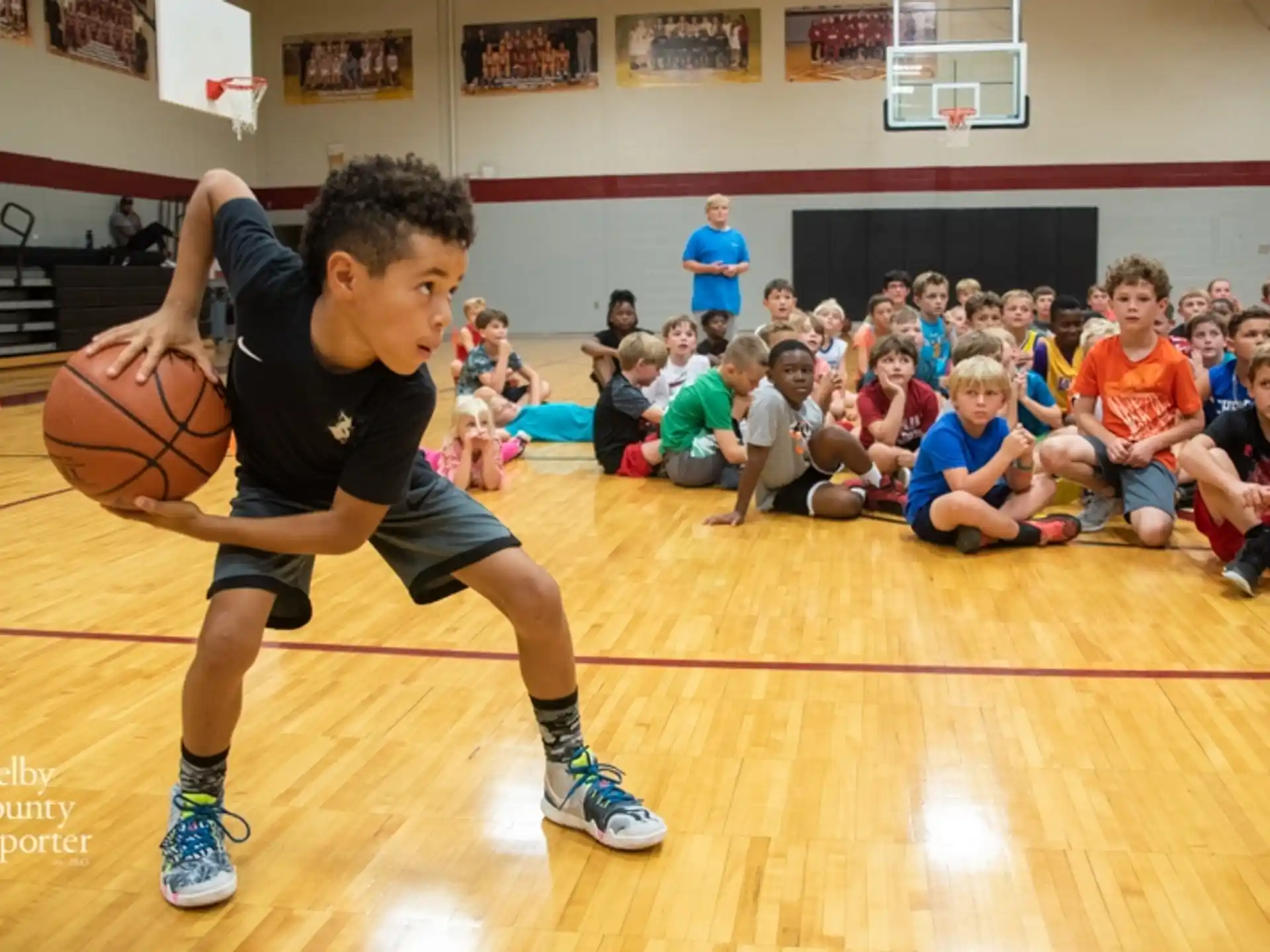 a boy playing basketball with a group of kids watching