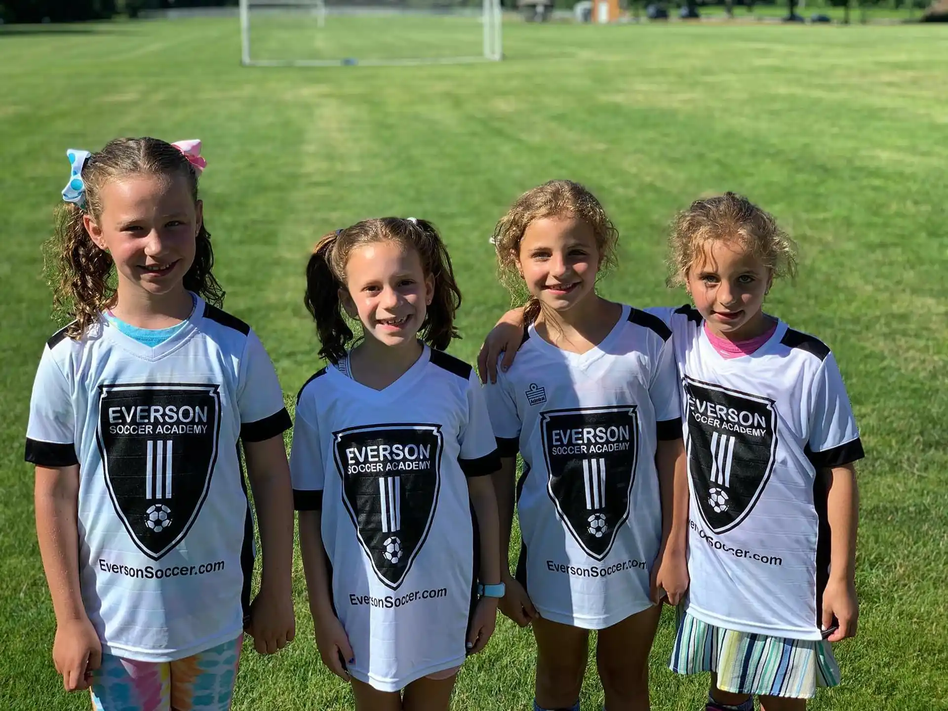 a group of girls in matching t-shirts standing in a grassy field