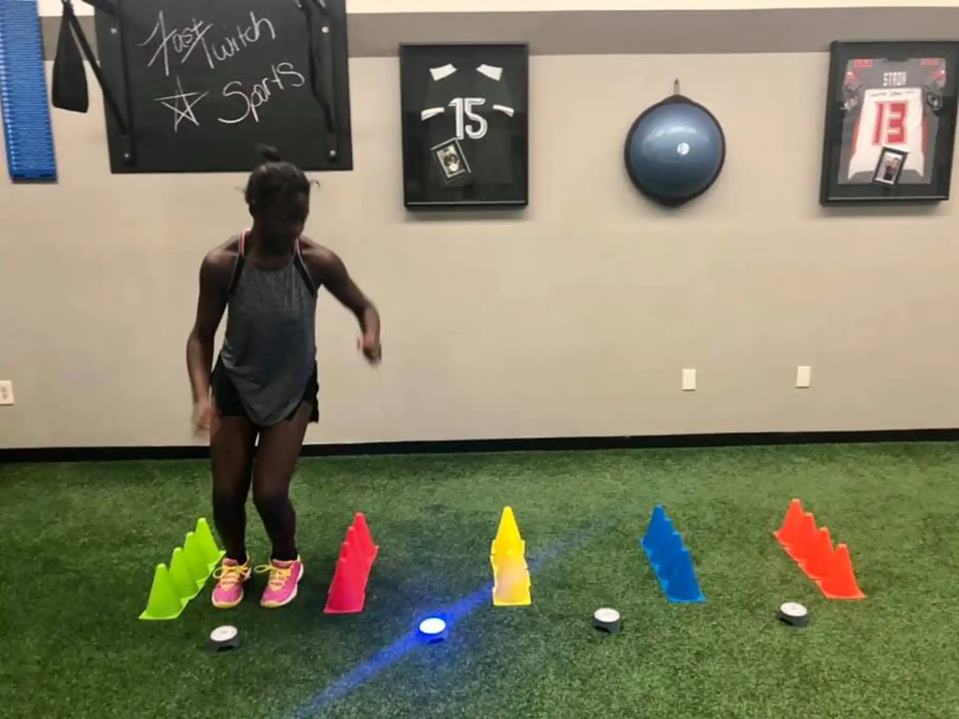 a girl standing on a green field with orange cones and a wall with pictures on it