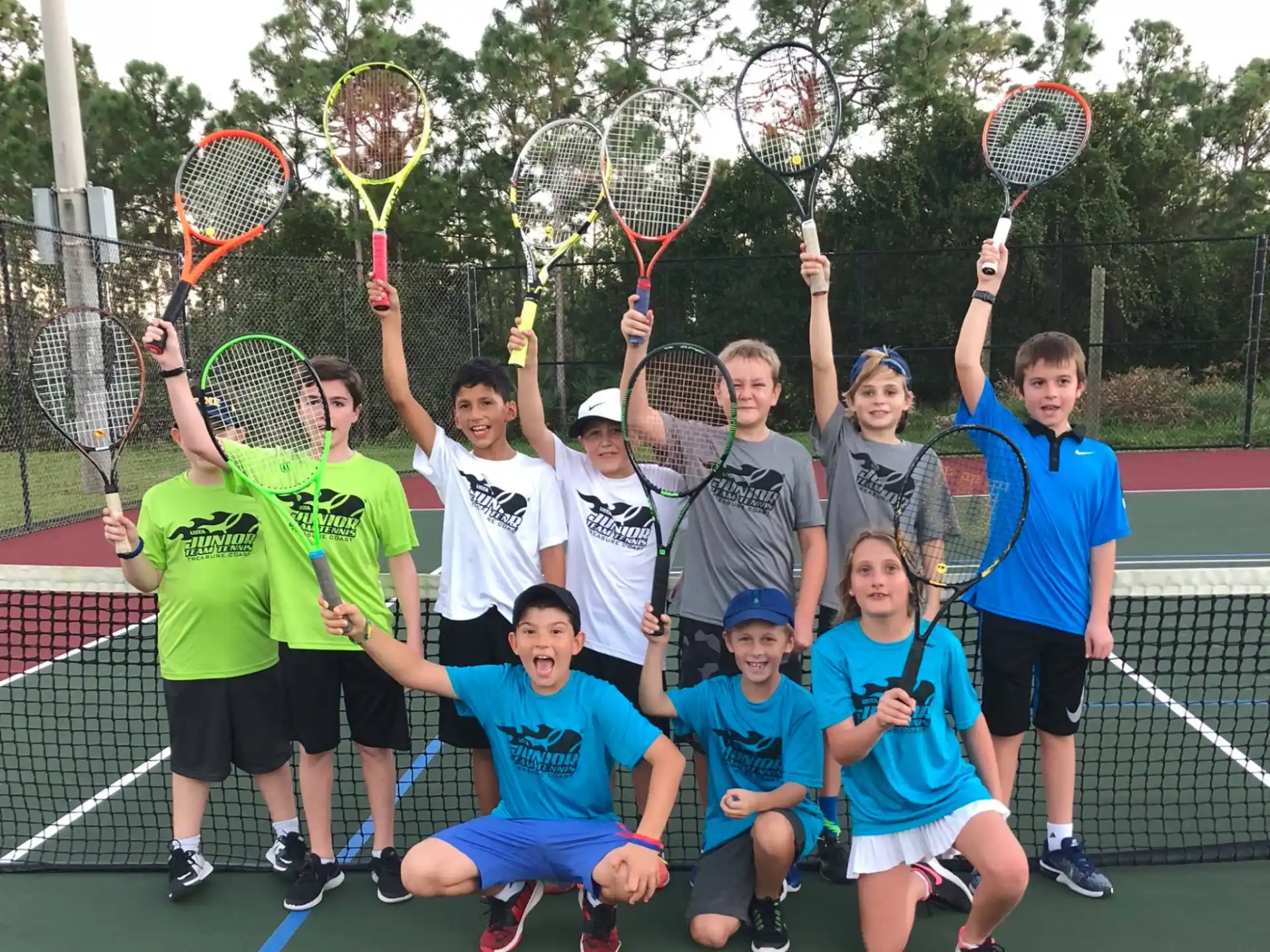 a group of kids pose for a photo with their tennis rackets