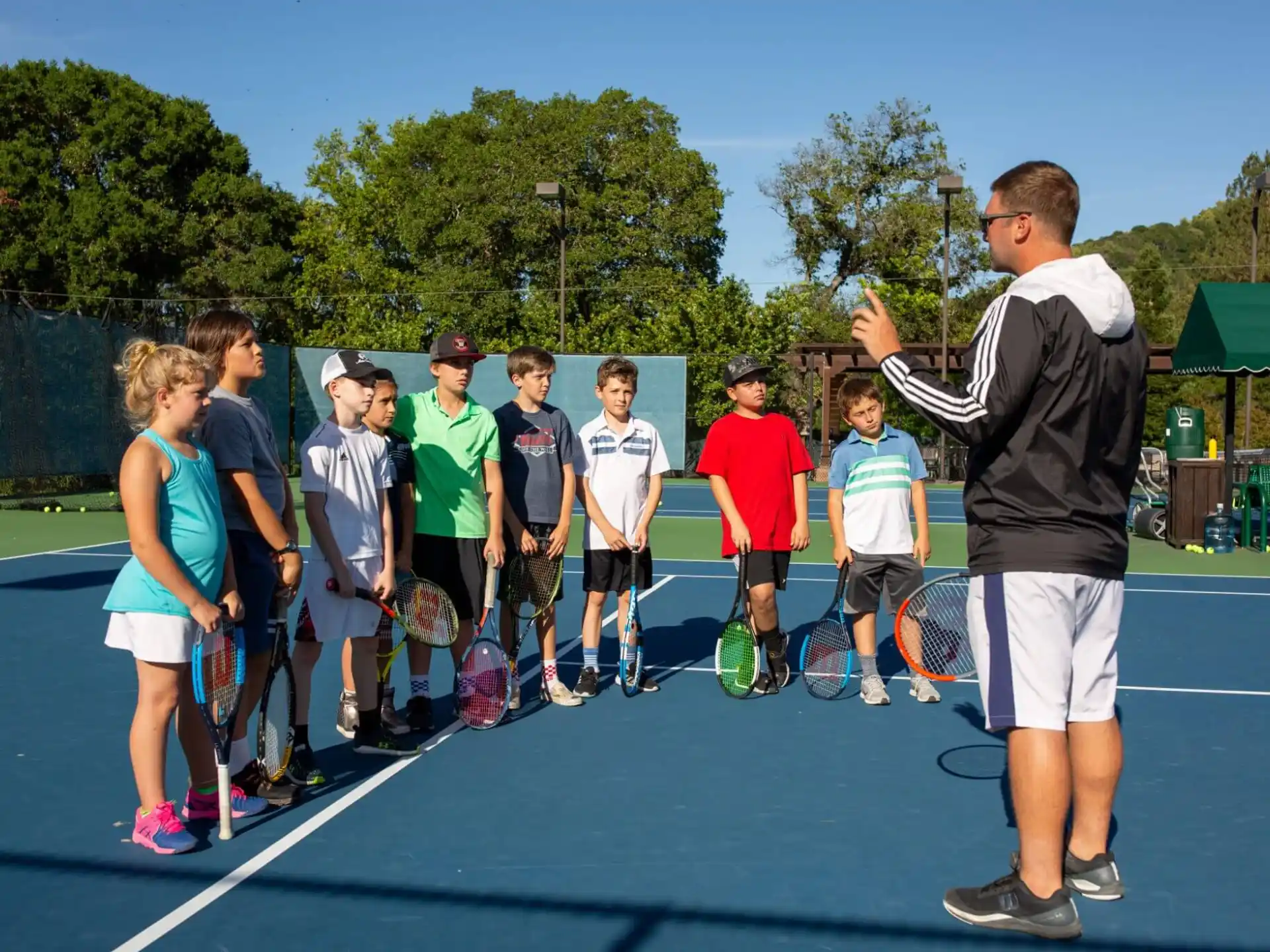 a person talking to a group of kids on a tennis court