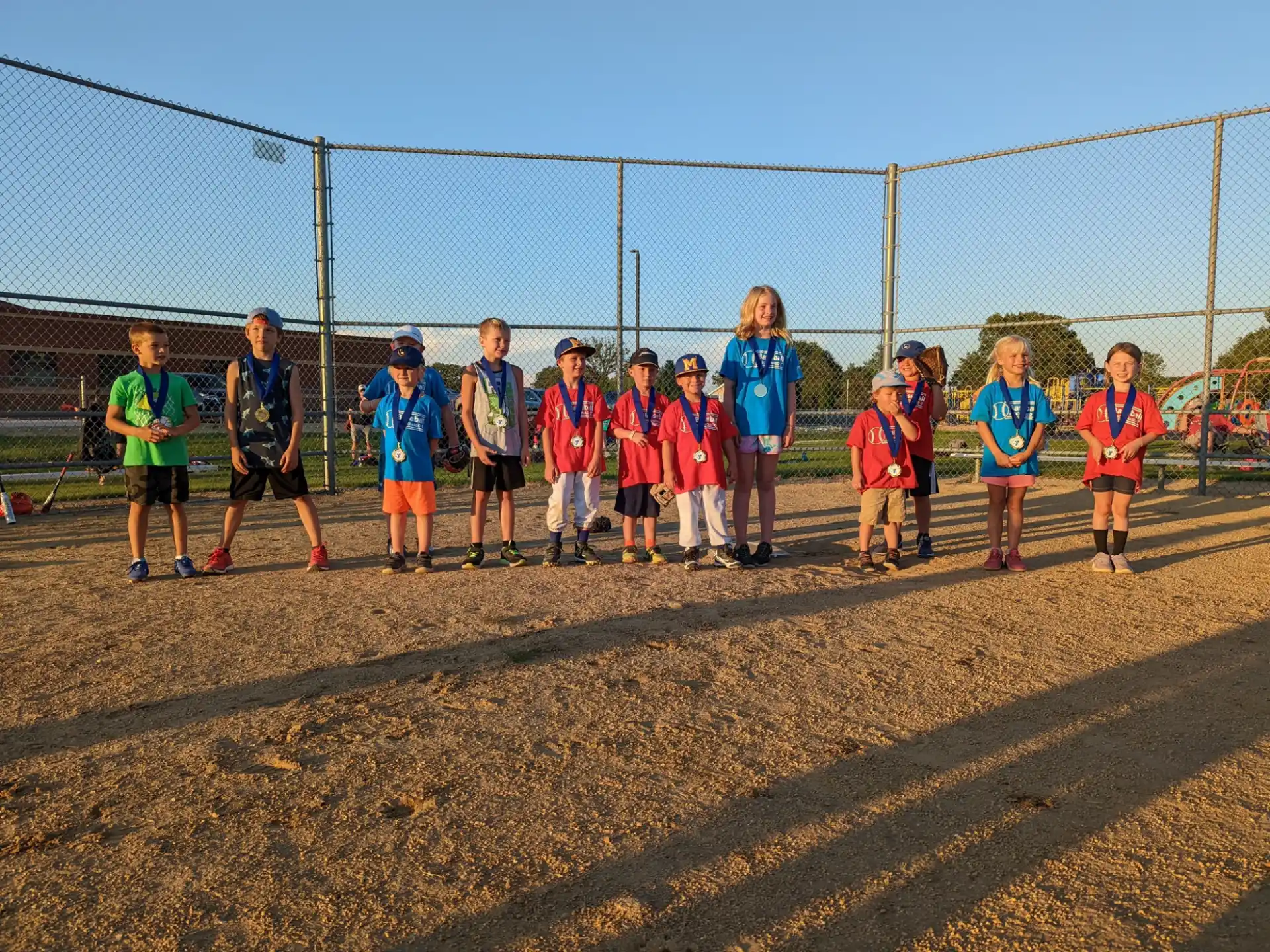 a group of children standing on a dirt road in front of a fence