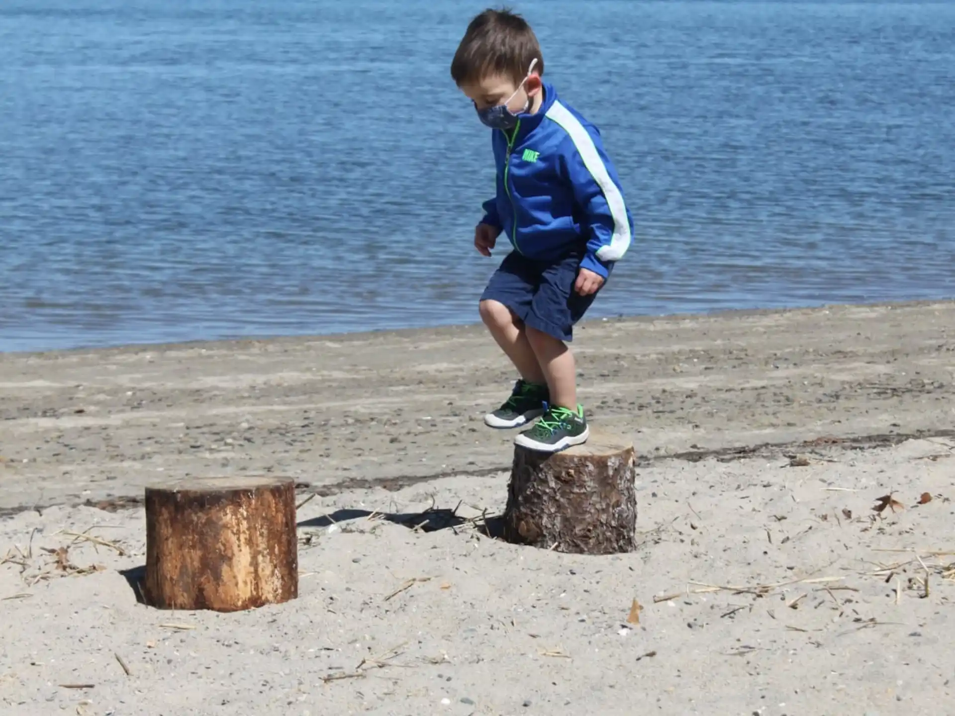 a boy jumping off a stack of wood on a beach