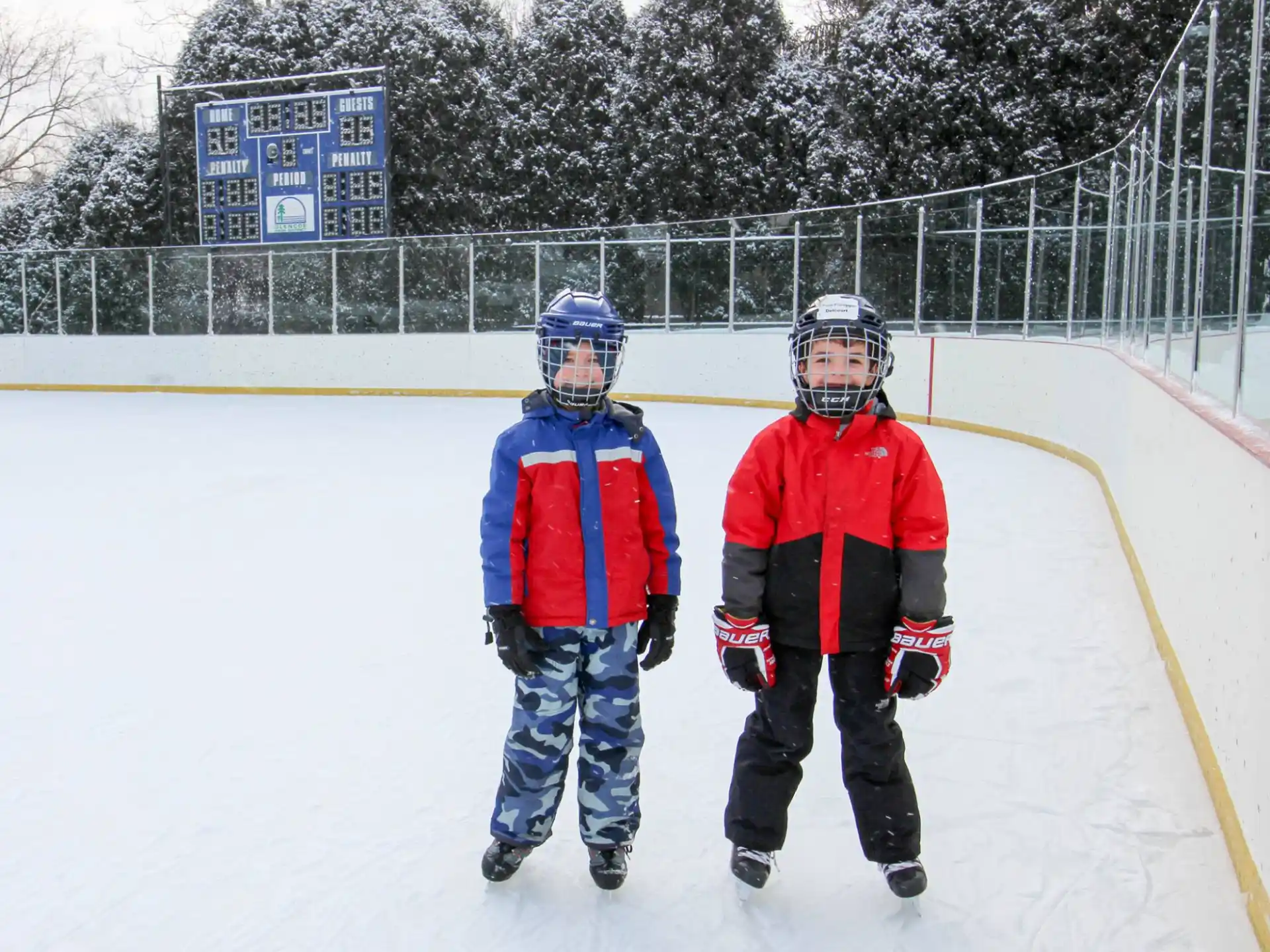 a couple of kids wearing helmets and ice skates on a snowy field
