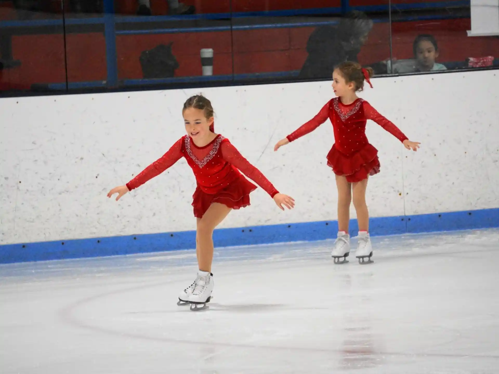 two girls wearing red uniforms and ice skates on an ice rink