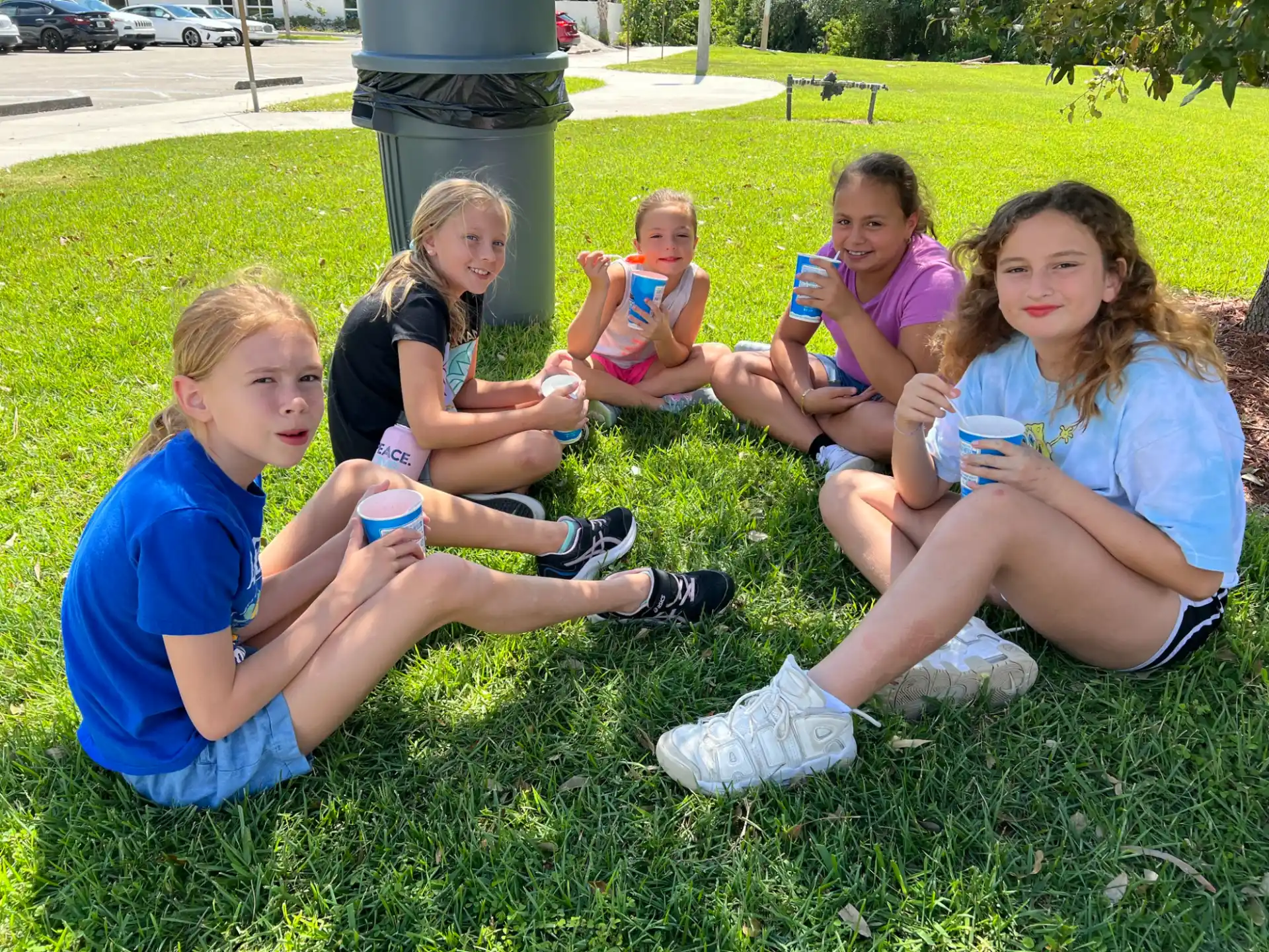 a group of girls sitting on the grass holding cups