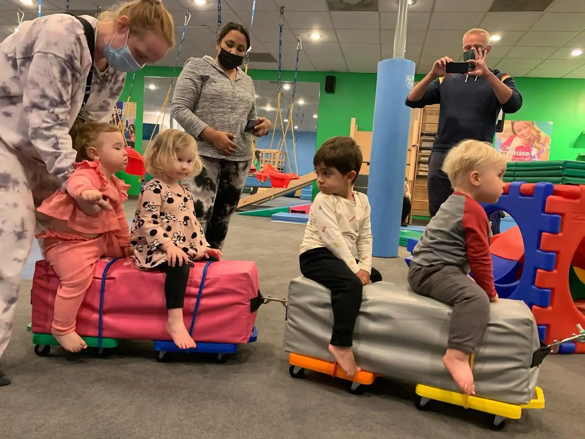 a group of children on toy skateboards in a room with people