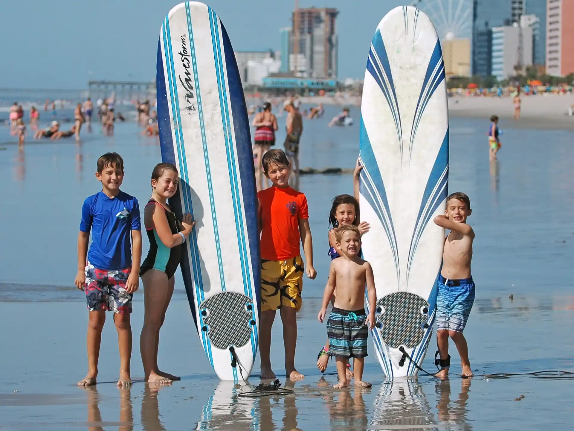 a group of kids stand on the beach with surfboards
