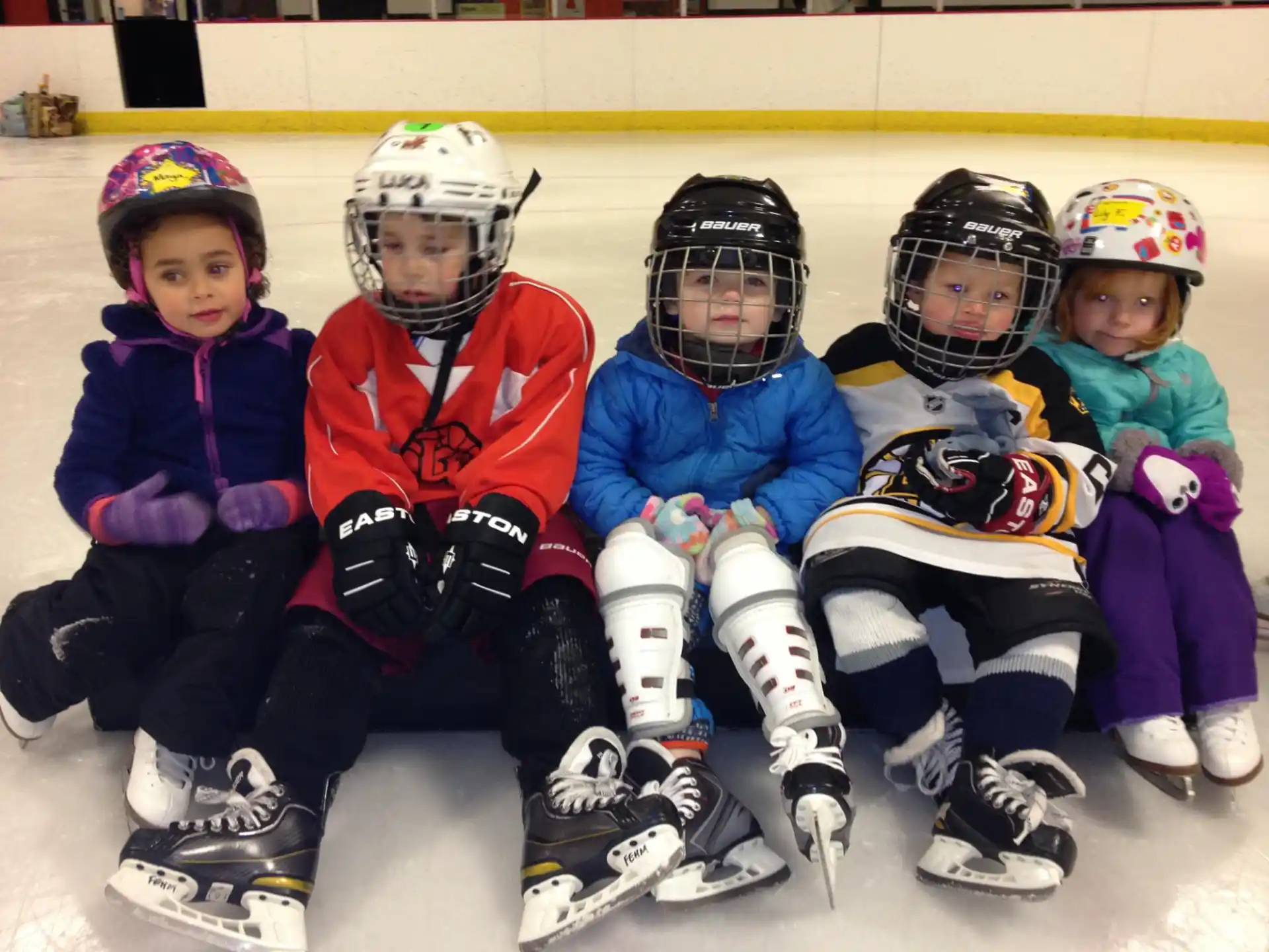 a group of kids wearing helmets and sitting on ice