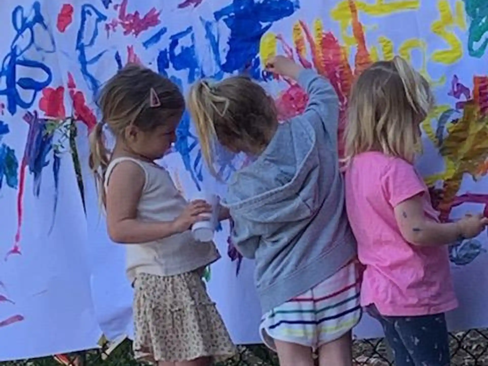 a group of children standing in front of a wall with a mural
