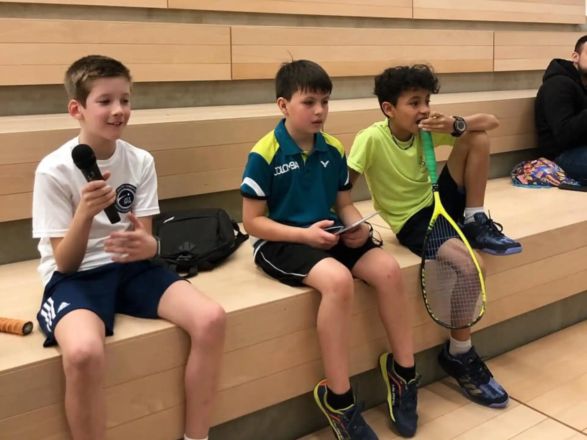 a group of boys sitting on a bench with tennis rackets