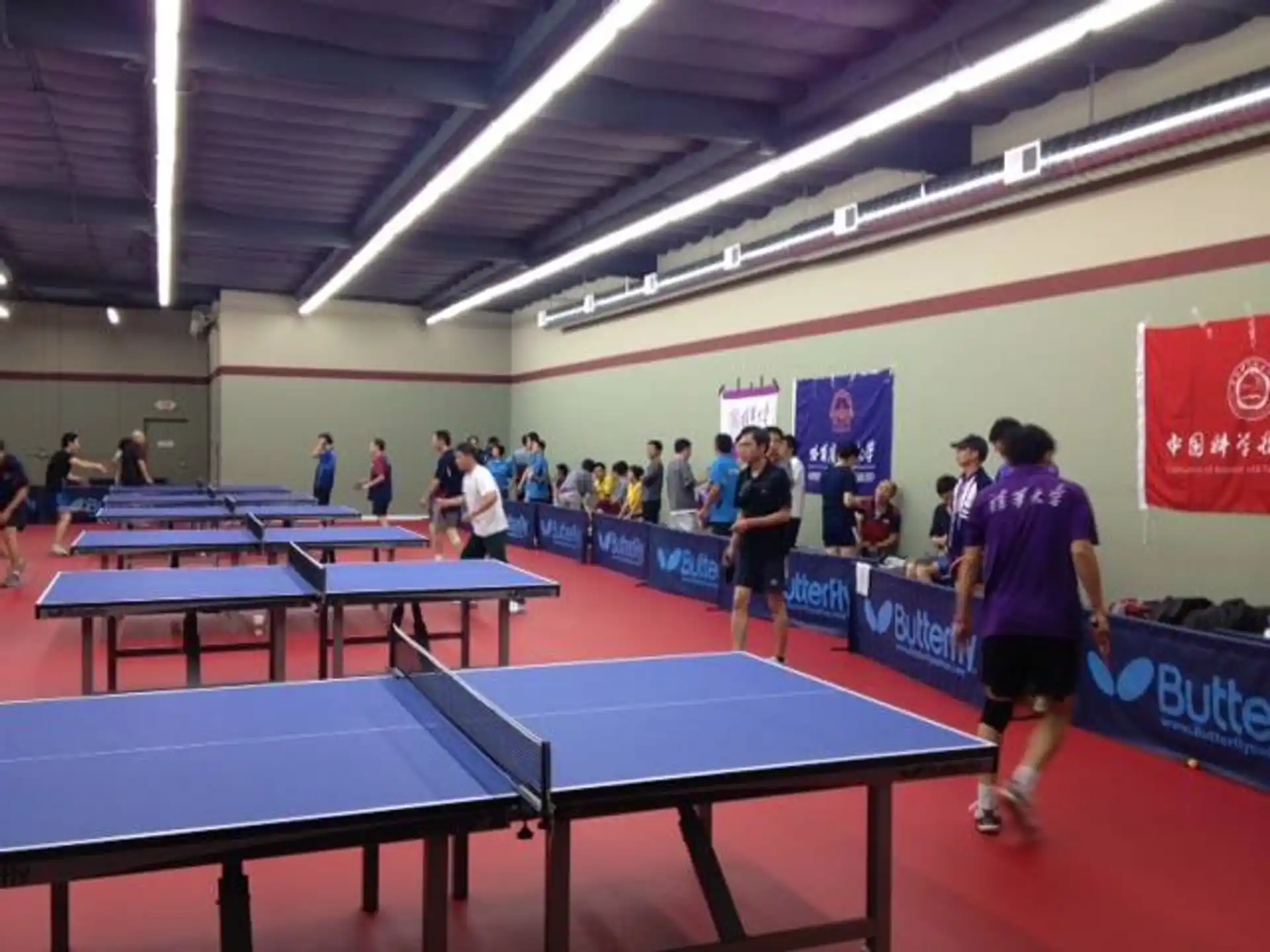 a group of people playing ping pong in a room with a blue wall and a red and