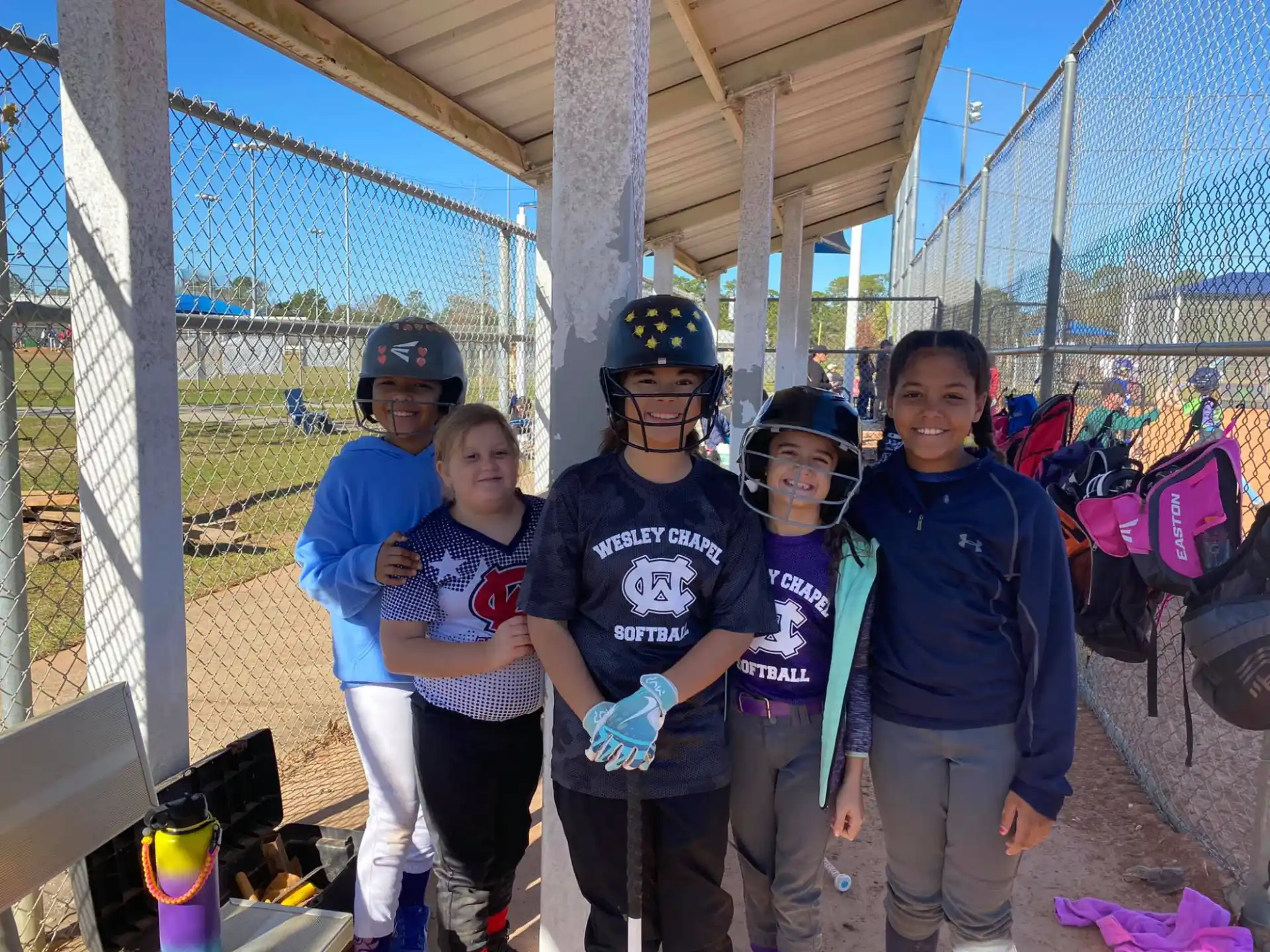 a group of kids wearing helmets and standing in front of a fence