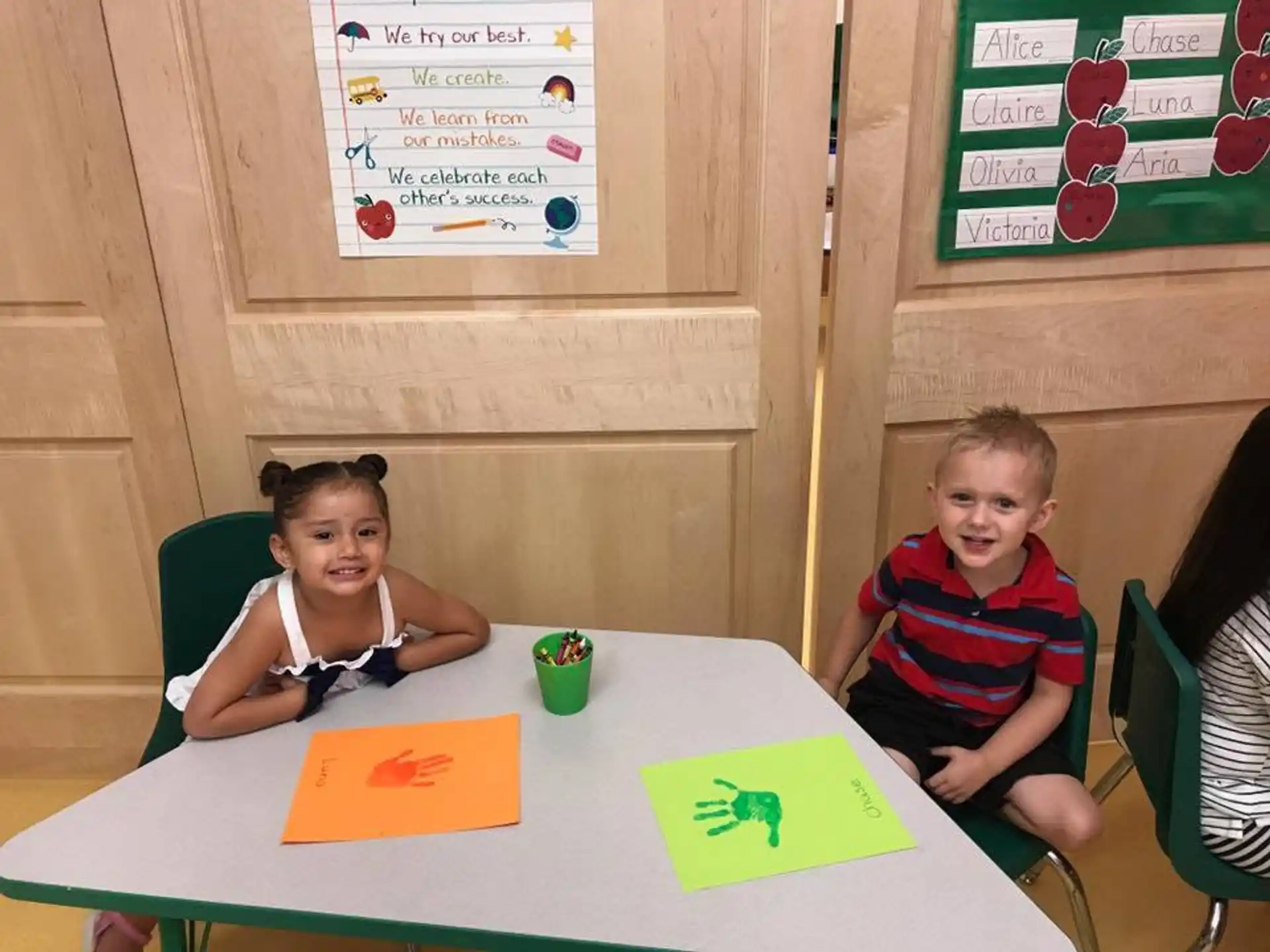 a couple of kids sitting at a table with a paper and a sign