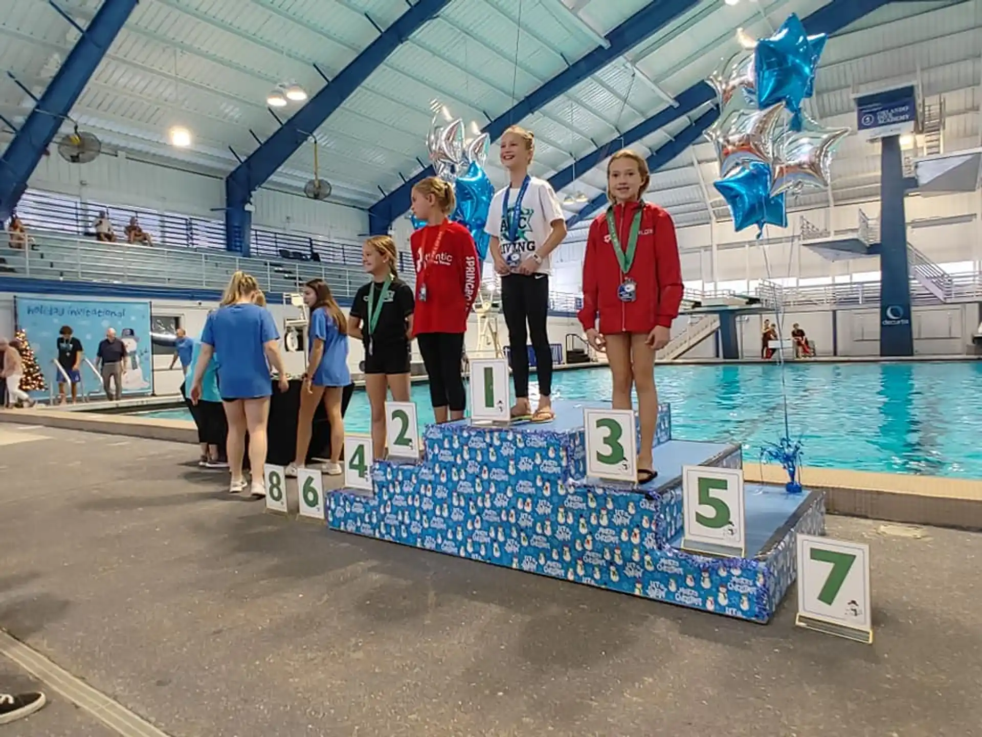 a group of people standing on a platform with medals and a pool