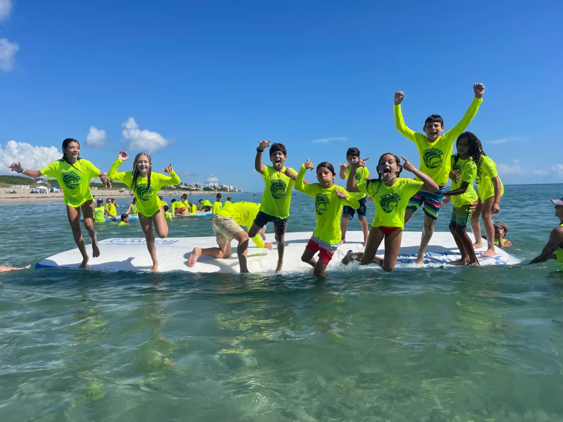 a group of people in green shirts jumping on a surfboard in the water