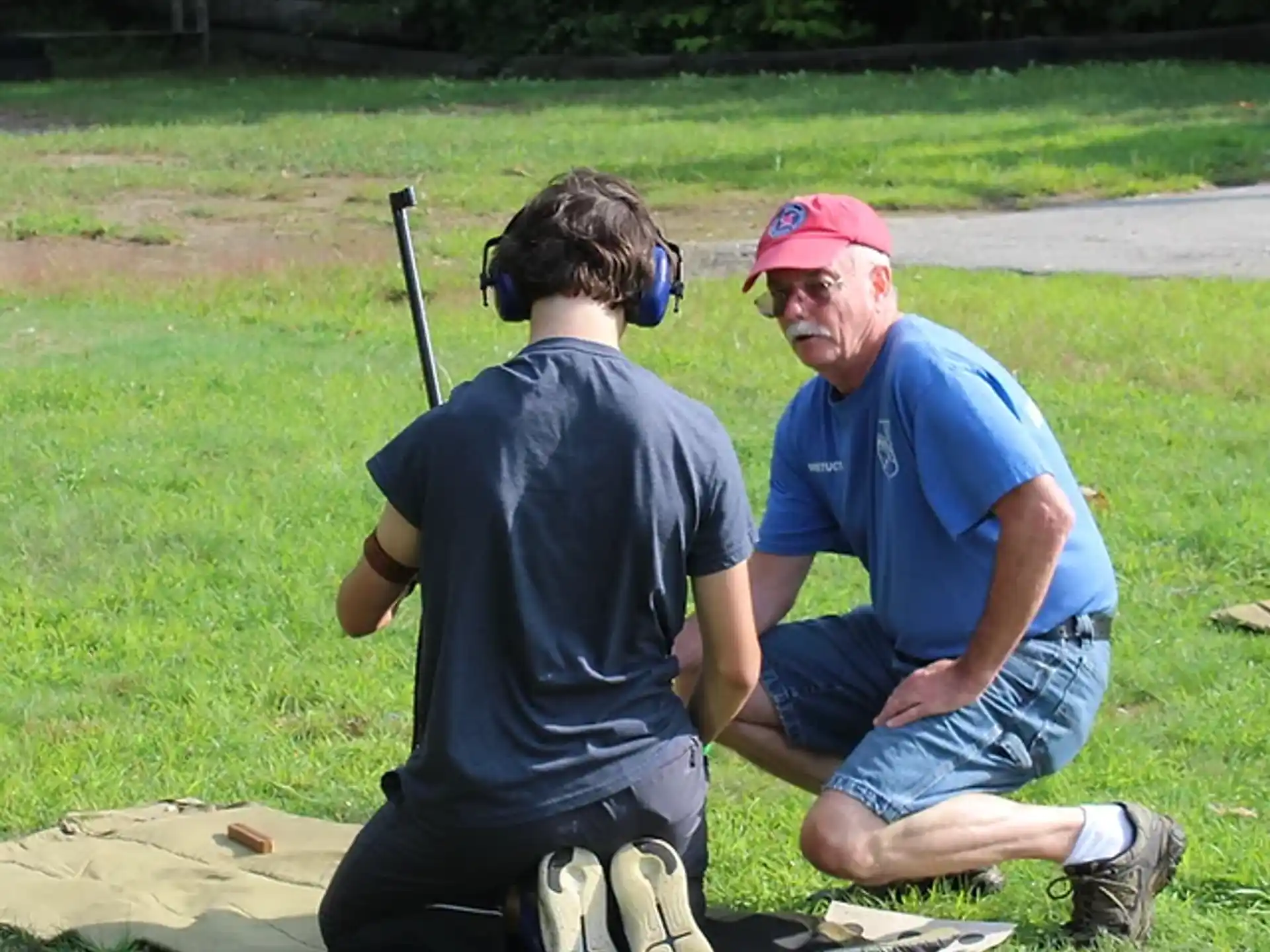 a couple of men sitting on the grass with a backpack and a helmet