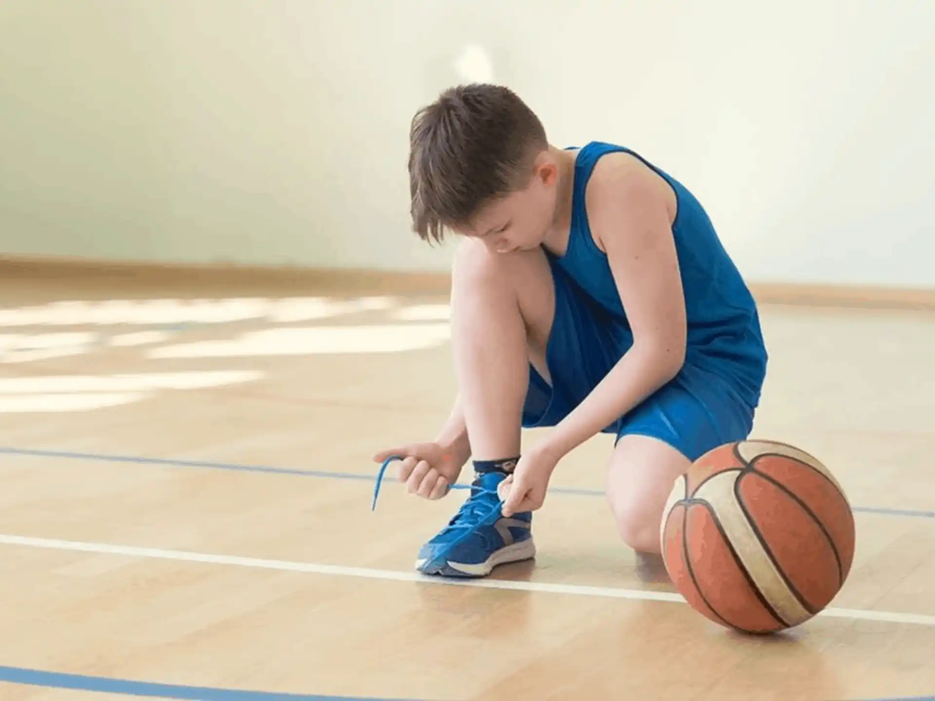 a boy kneeling on the floor with a basketball
