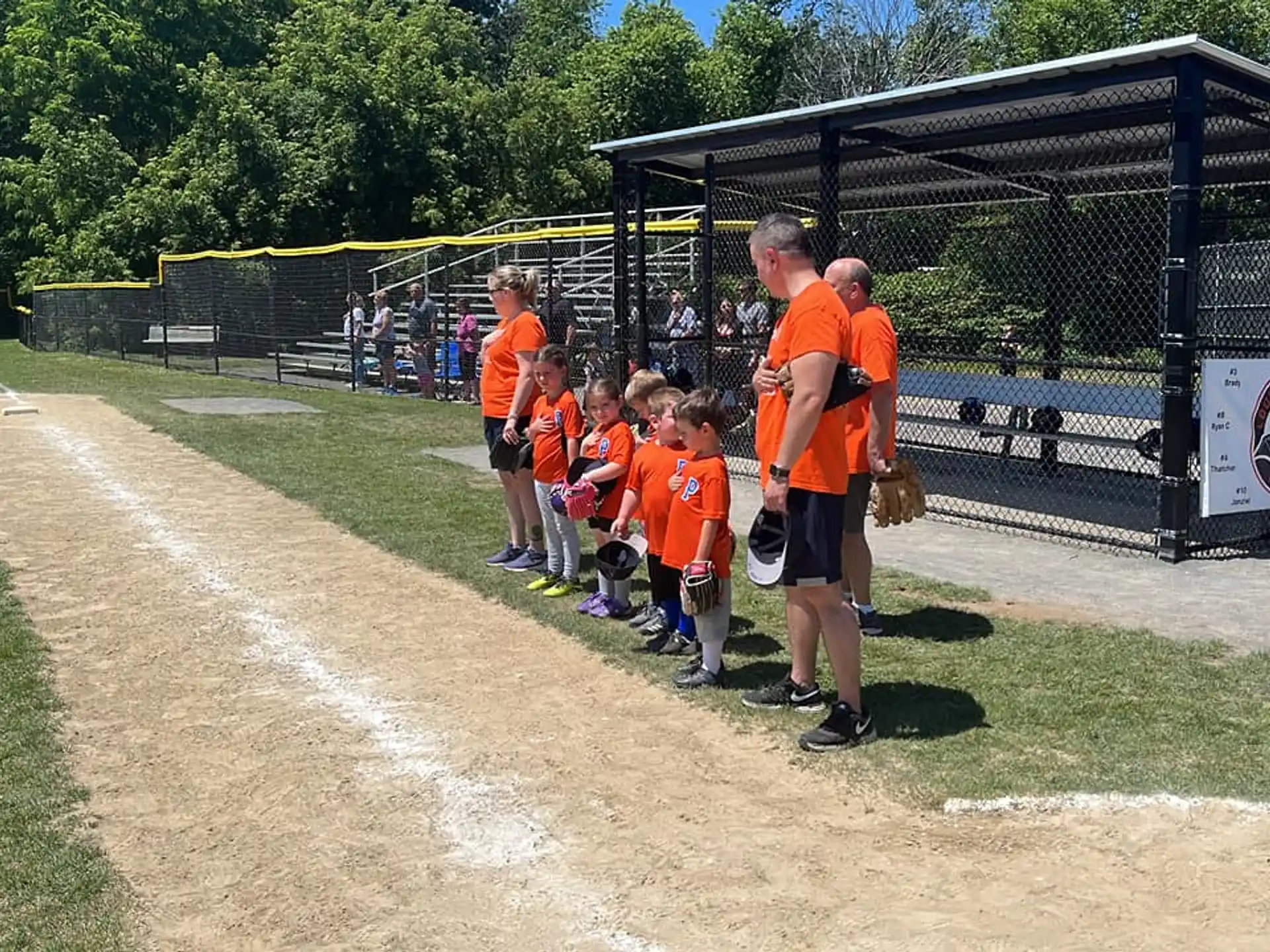 a group of kids in orange shirts standing on a baseball field