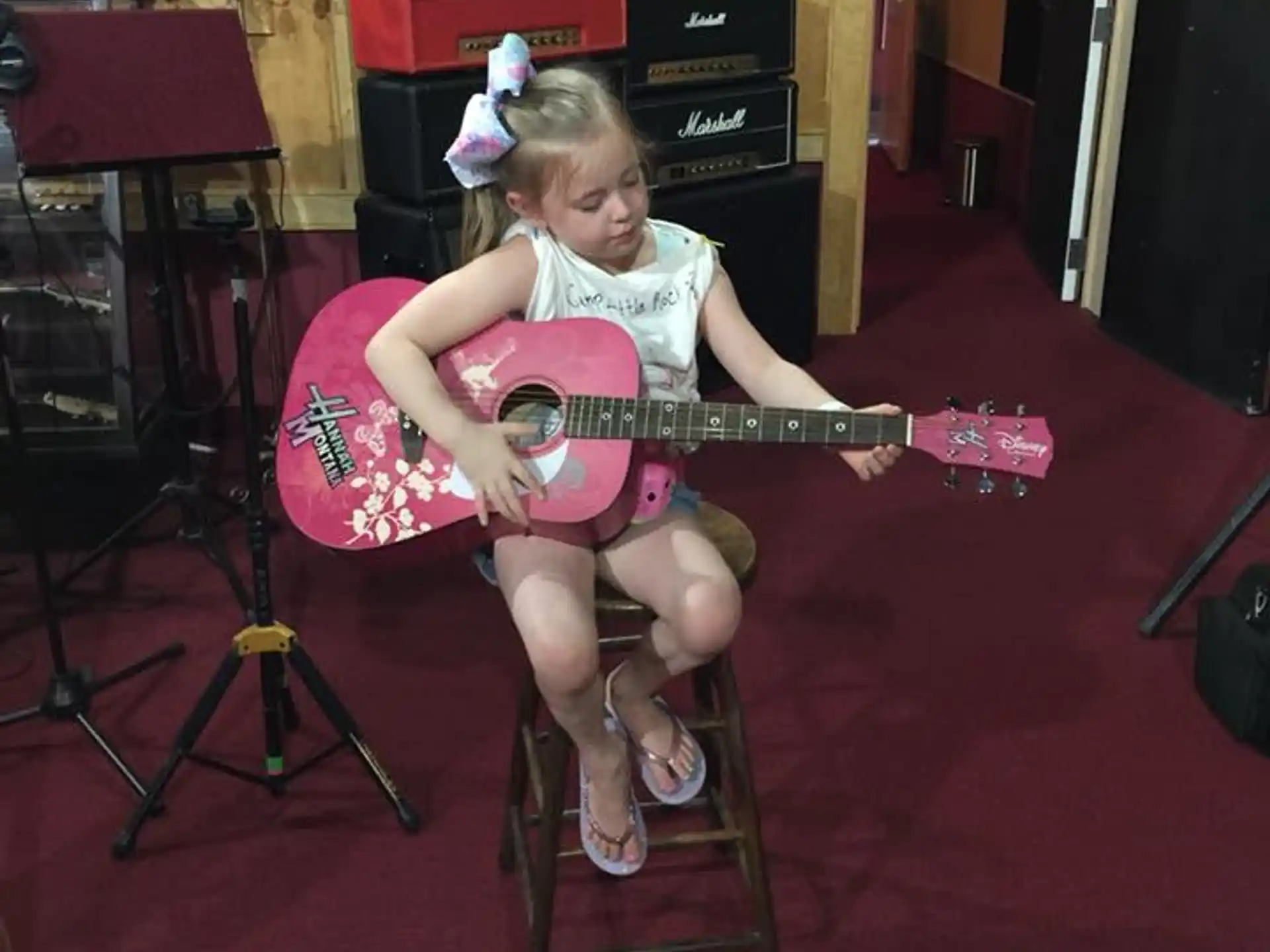 a girl sitting on a stool playing a guitar