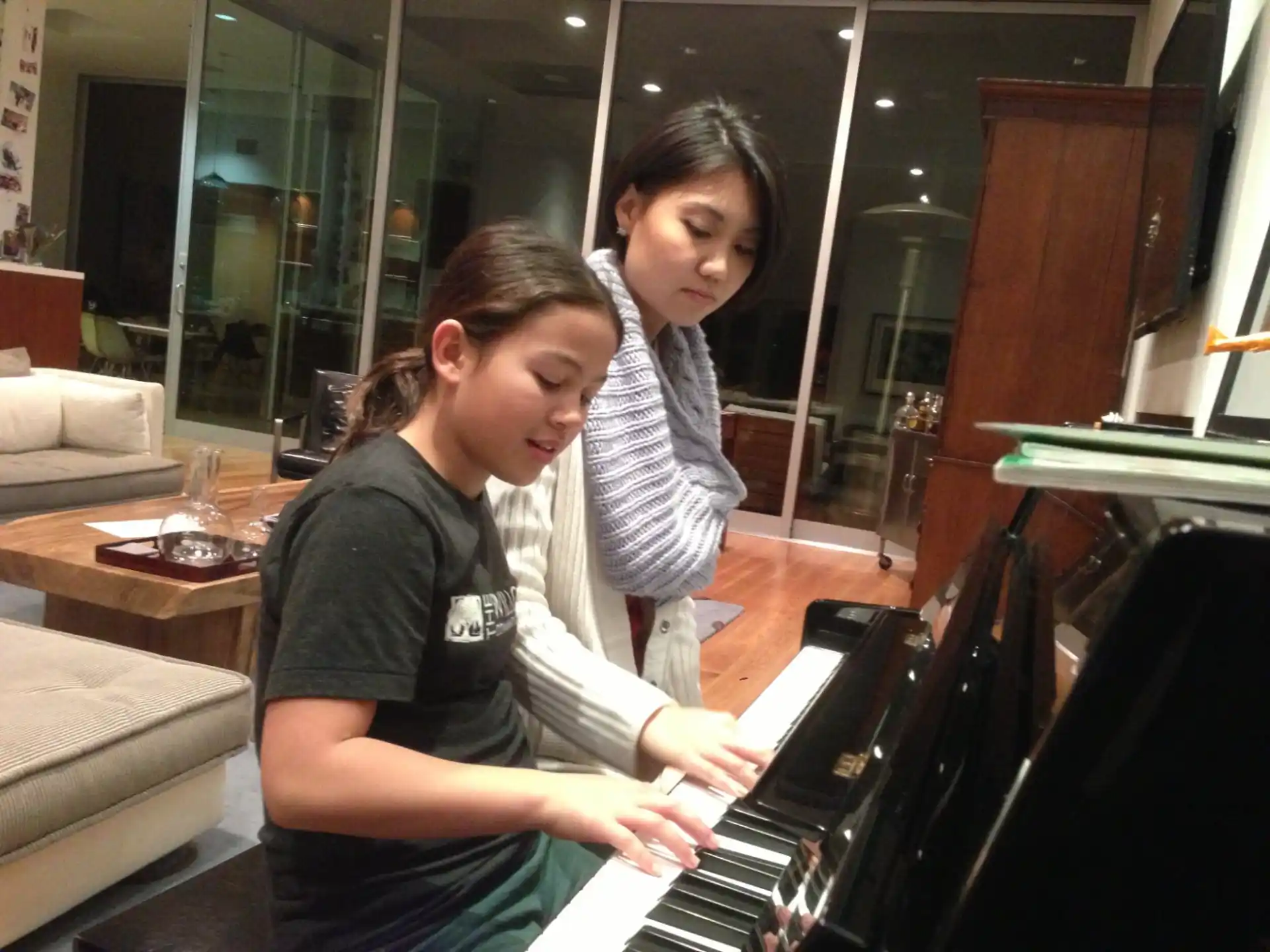a person playing a piano with a young girl standing behind the