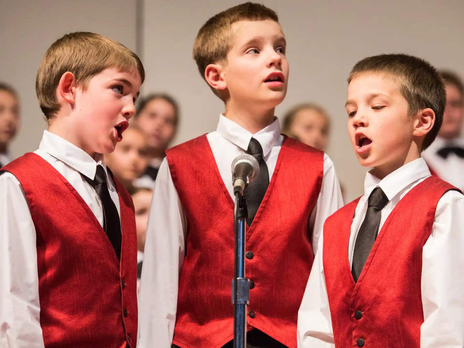 a group of boys in red and white uniforms singing into microphones