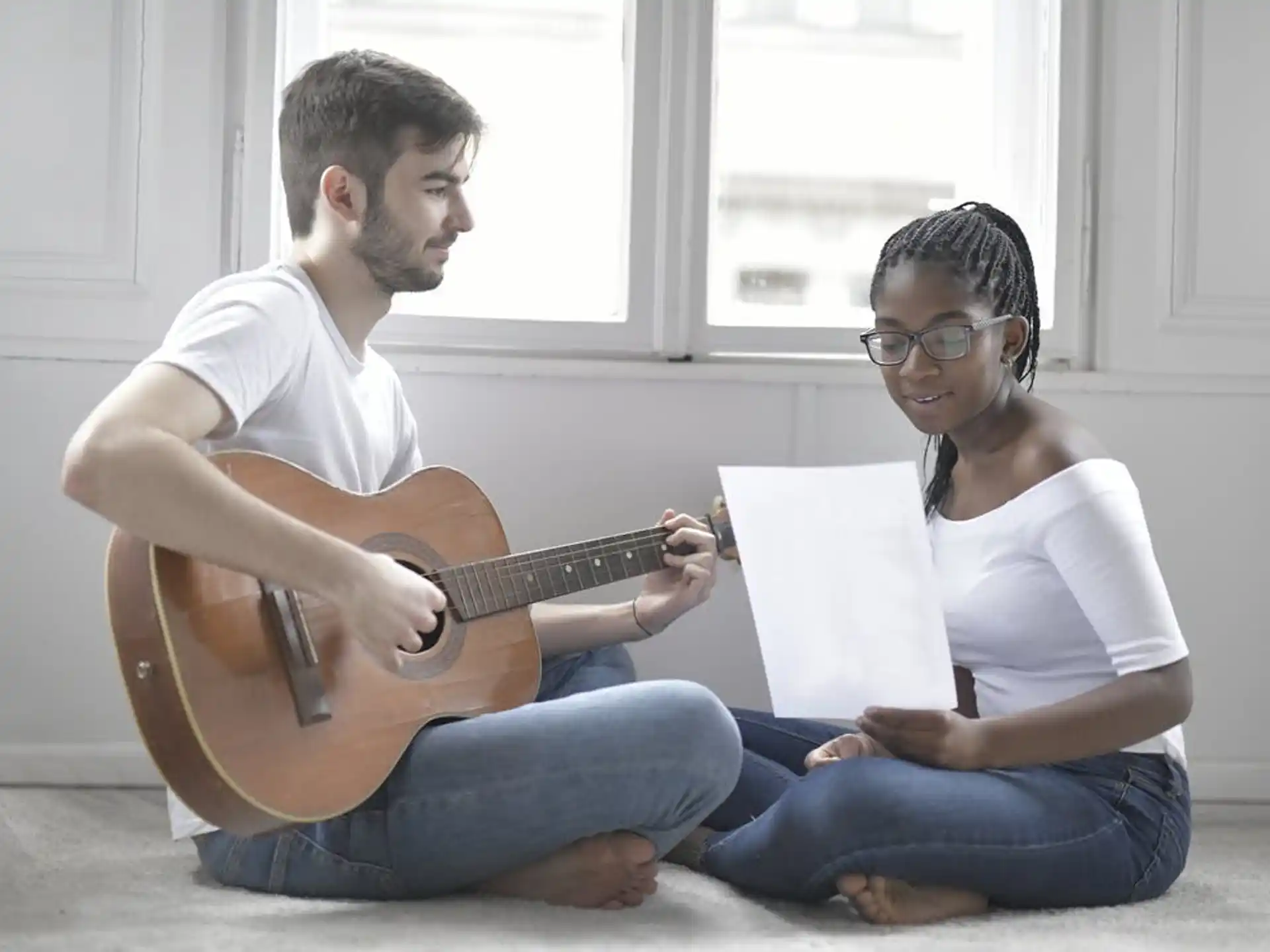 a man and a woman sitting on the floor playing a guitar