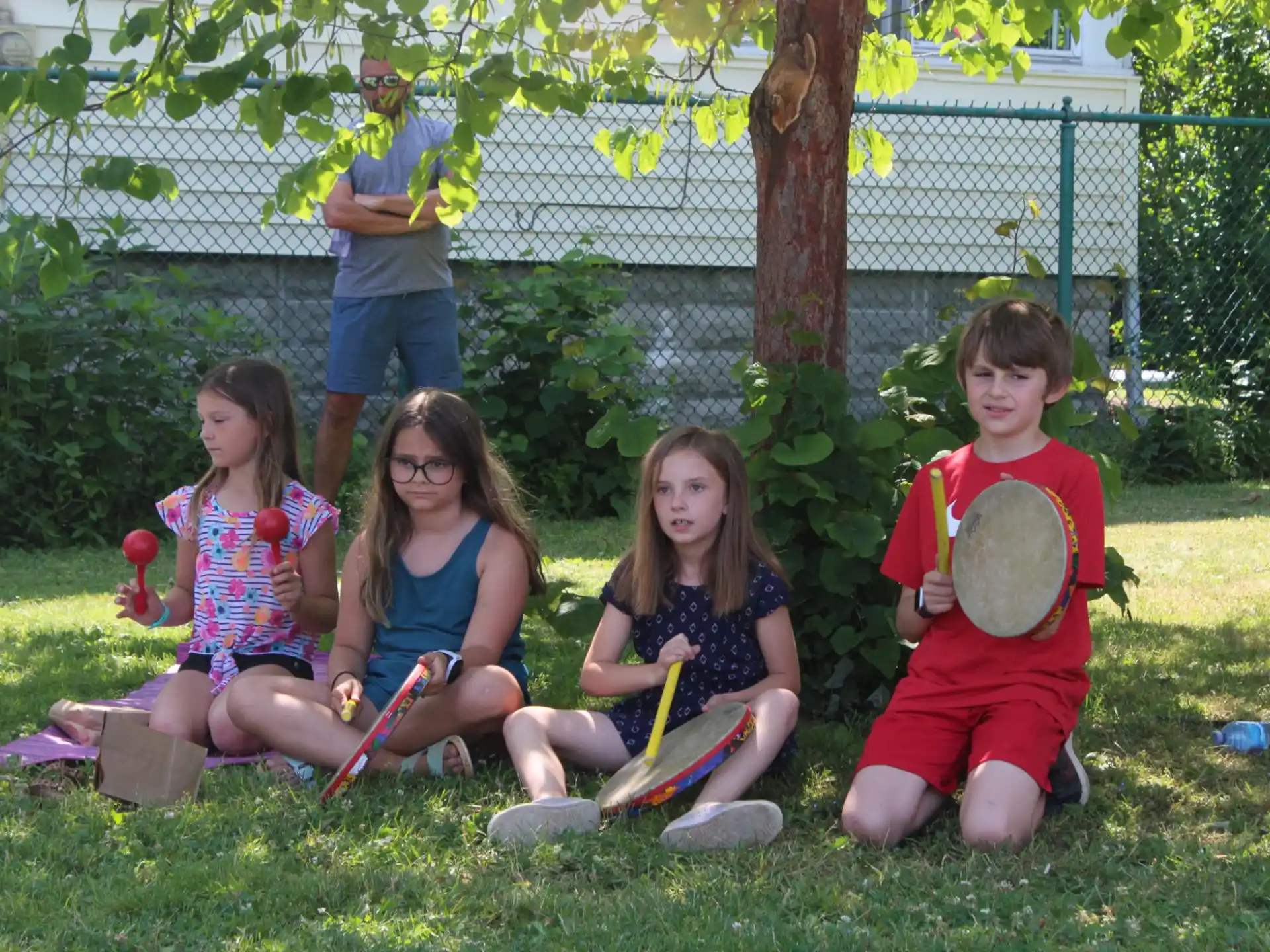 a group of kids sitting on the grass with instruments
