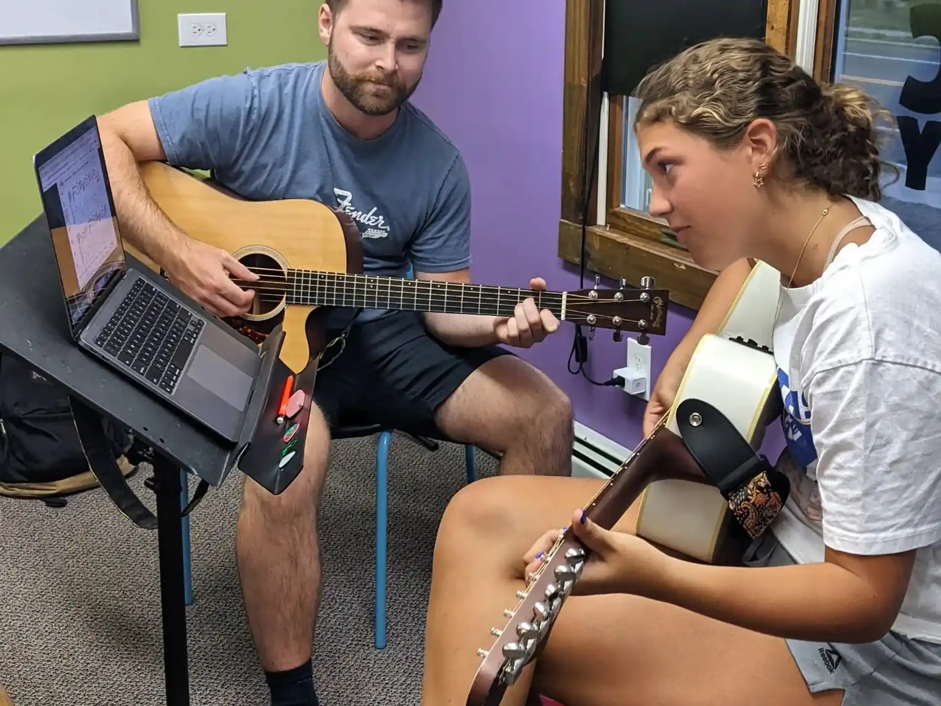 a man playing guitar next to a woman sitting on a chair