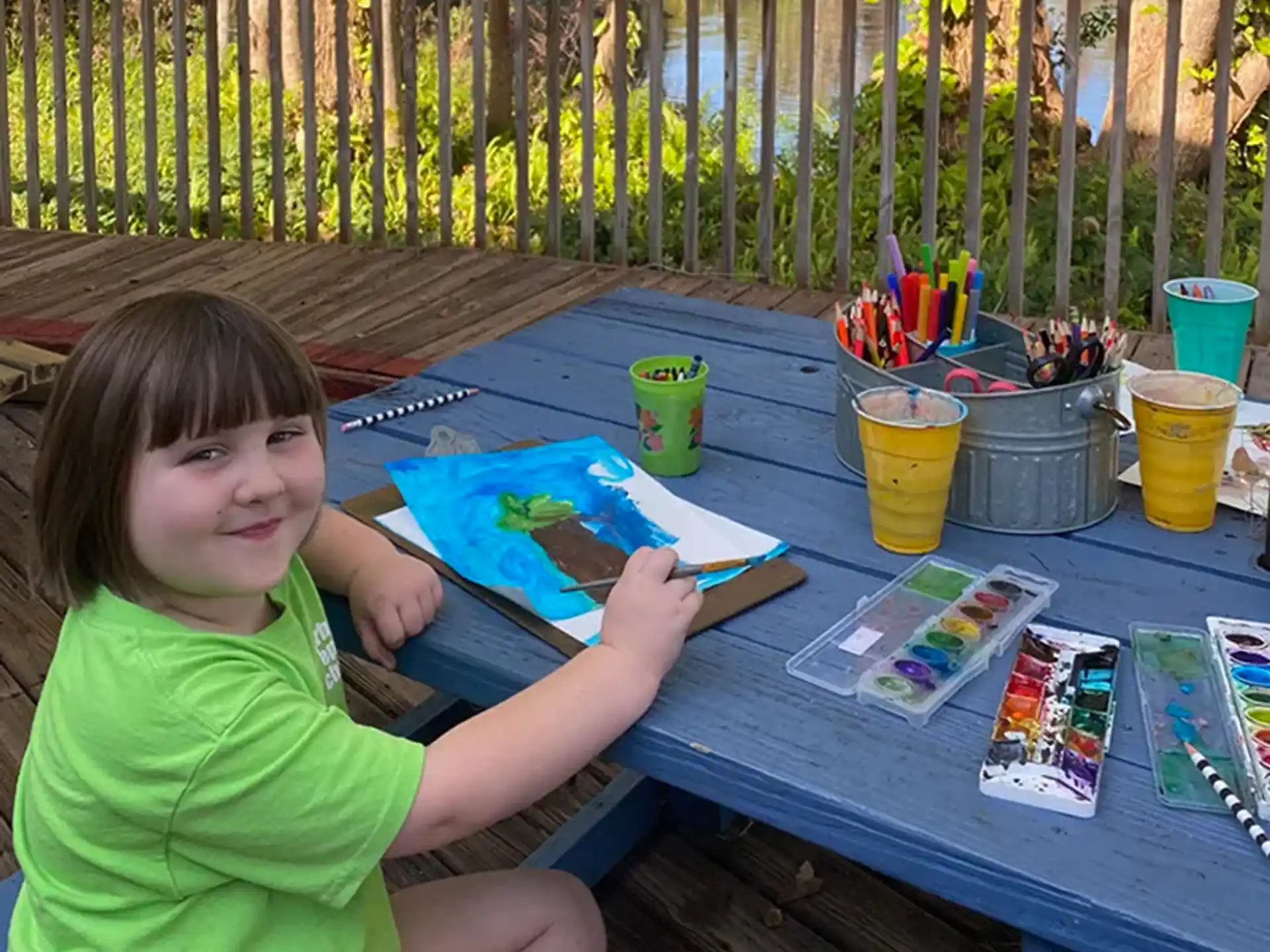 a girl sitting at a table with a painting and cups