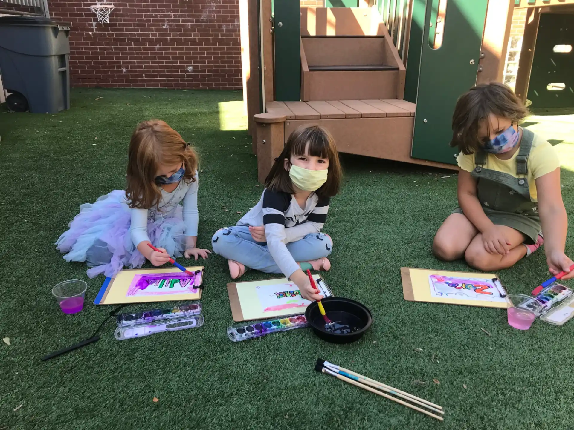 a group of children sitting on the grass with paper on the ground