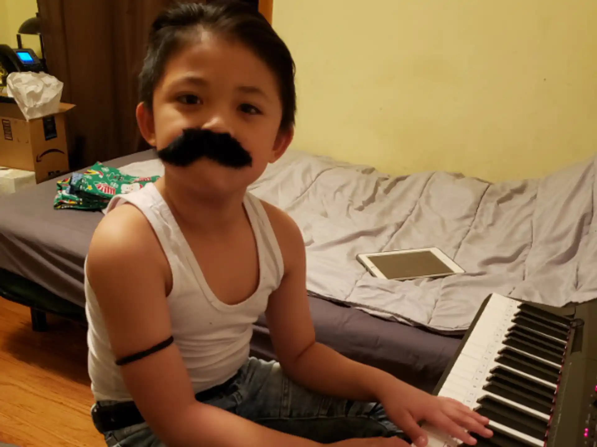 a boy with a mustache sitting on a bed with a keyboard