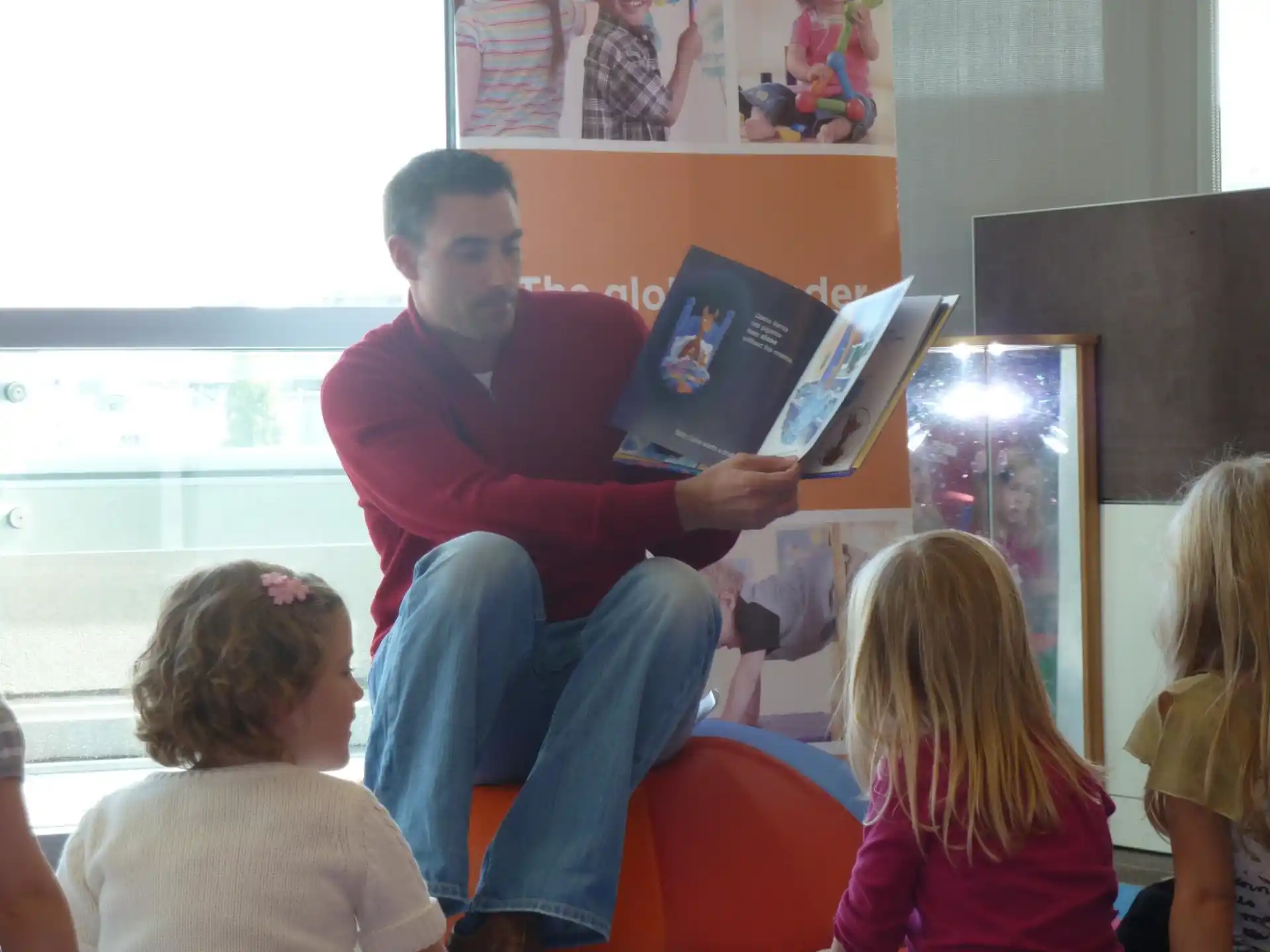a person sitting in a chair reading a book to a group of children
