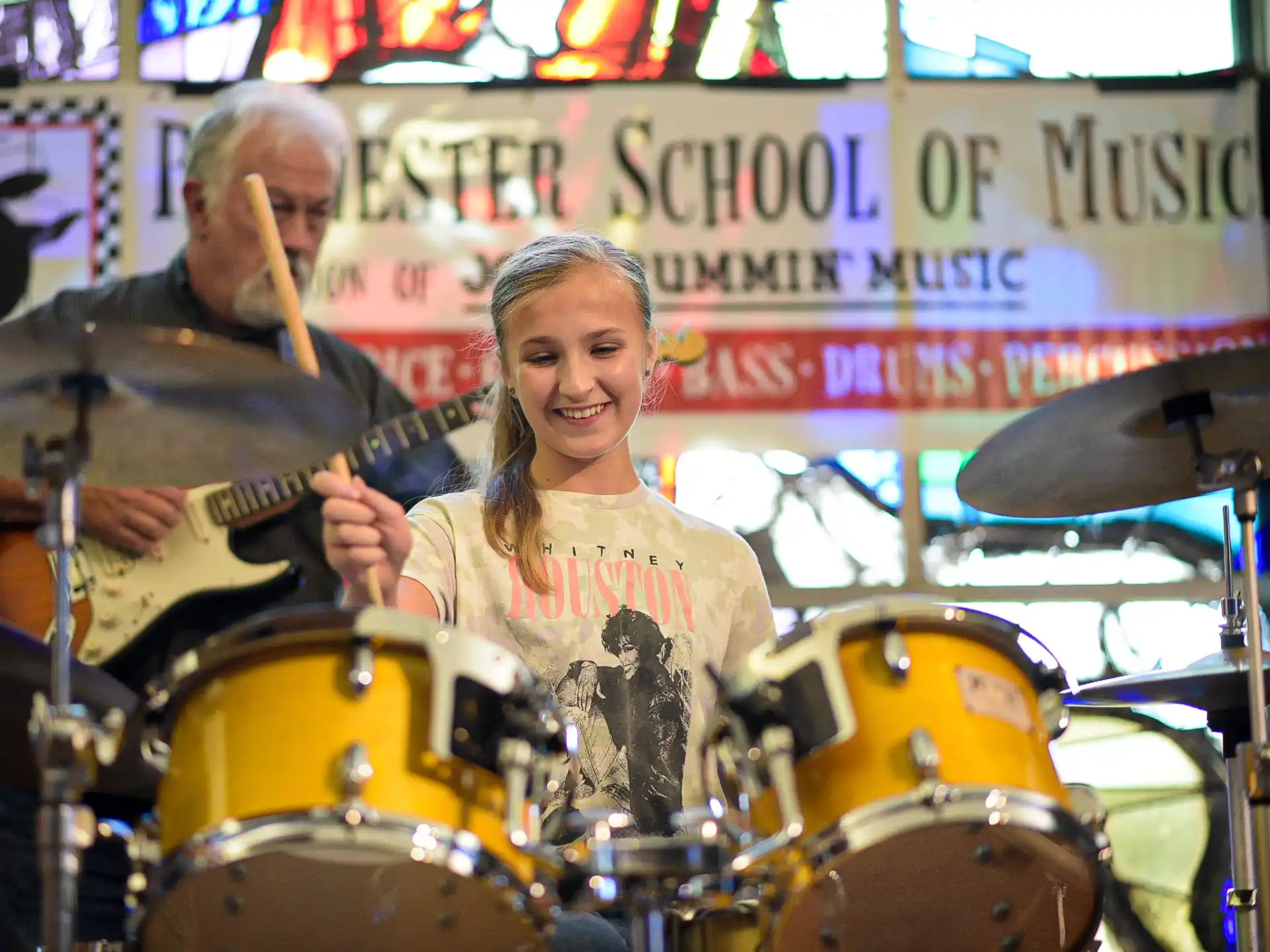 a woman playing a guitar next to a man playing drums