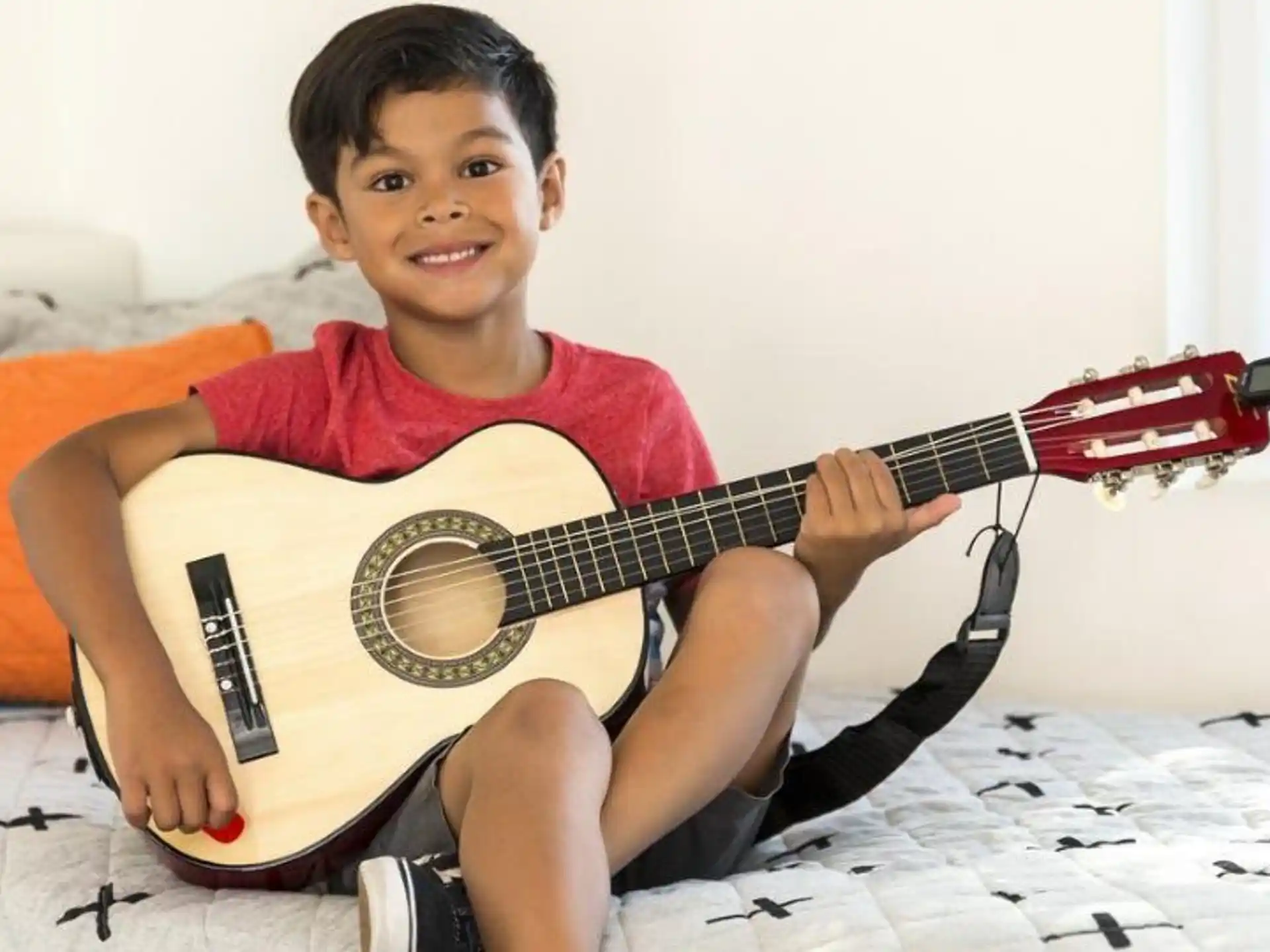 a boy sitting on a bed playing a guitar