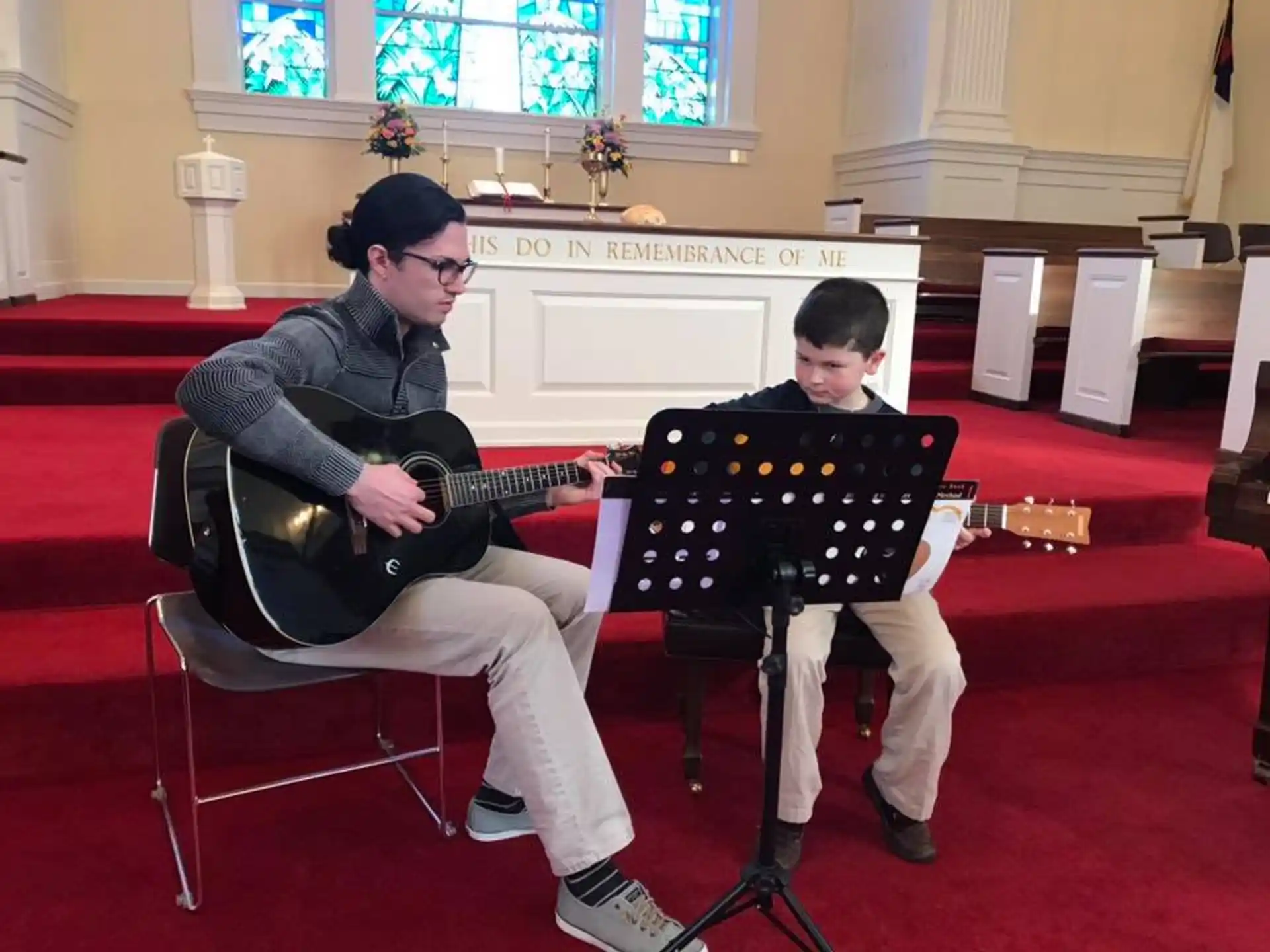 a person playing guitar next to a boy sitting in a chair