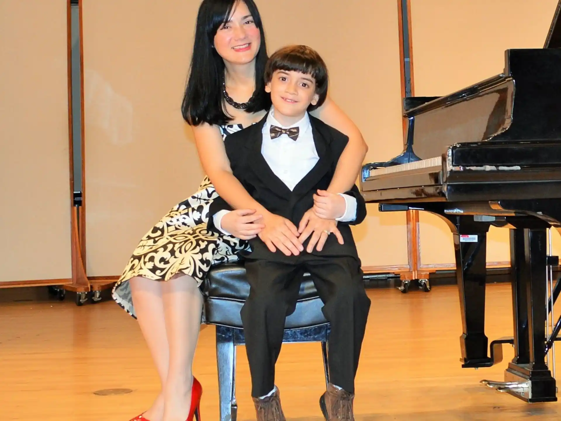 a boy and girl sitting on a chair in front of a piano