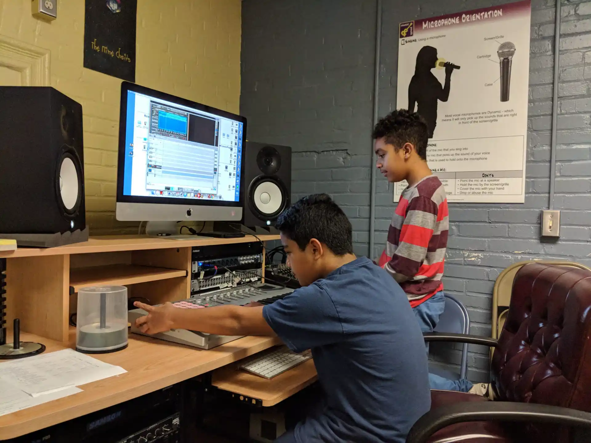 a couple of men sitting at a desk with a computer and speakers