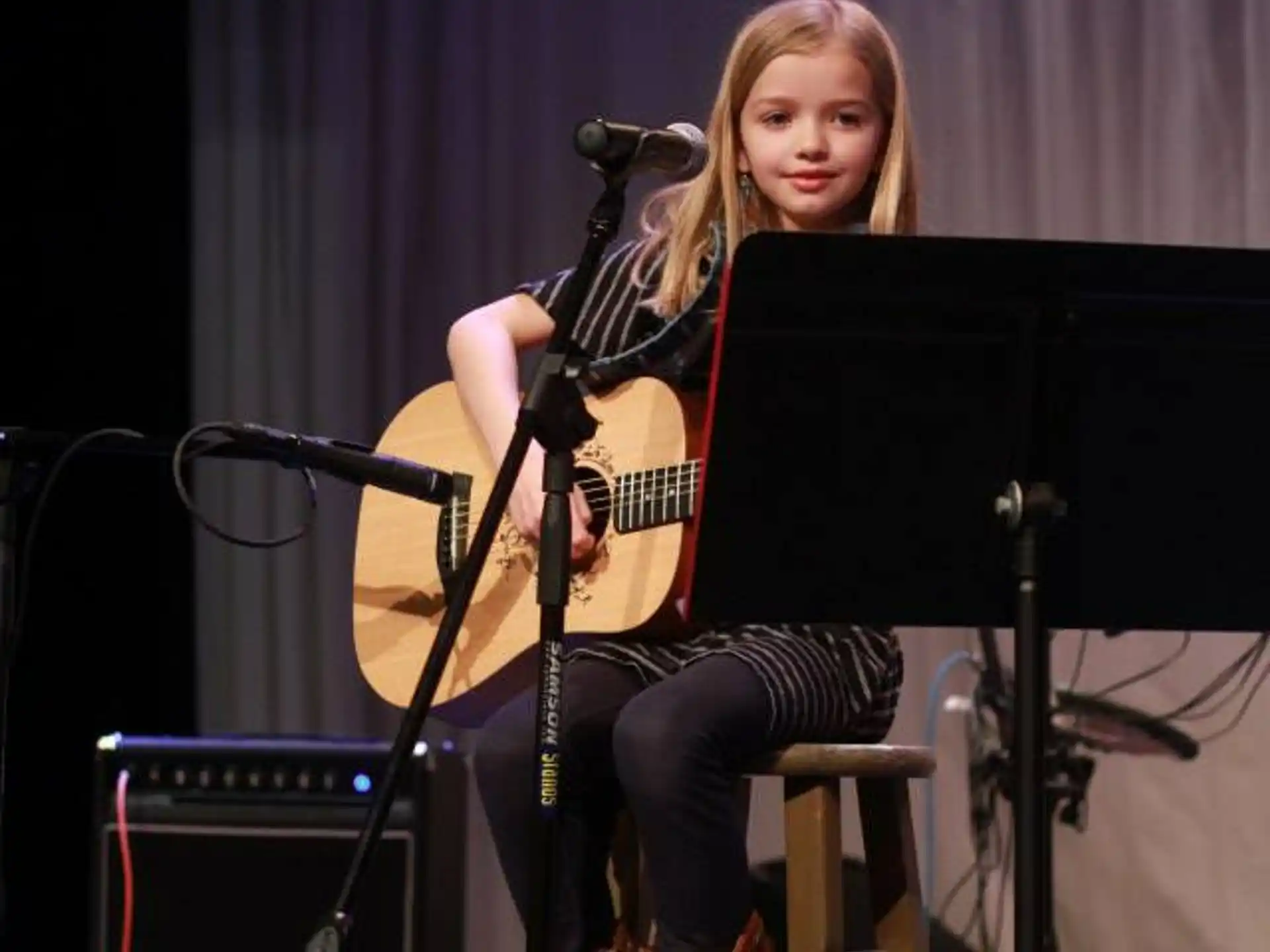 a woman sitting on a stool playing a guitar