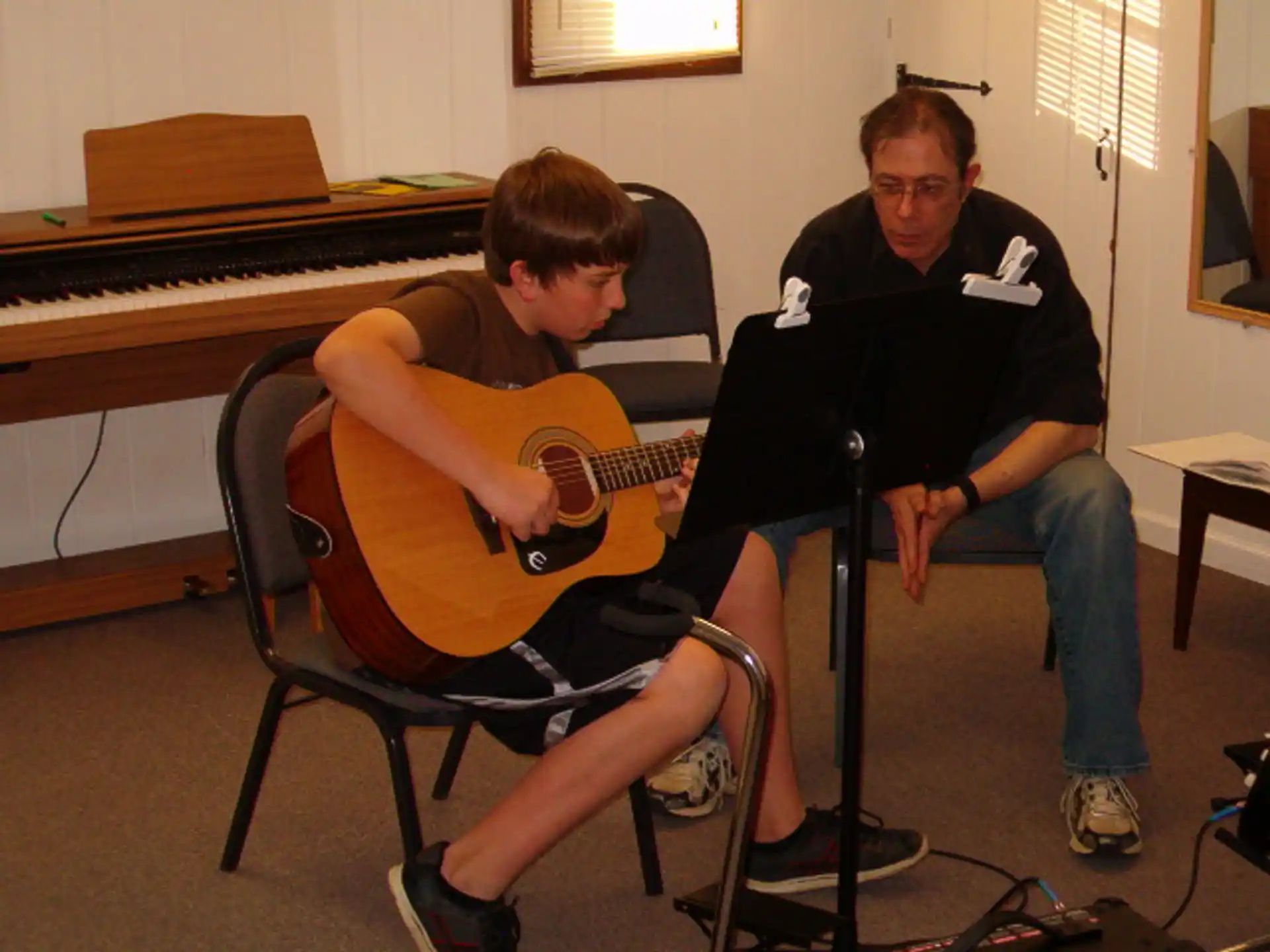a man playing a guitar next to a boy sitting on a chair