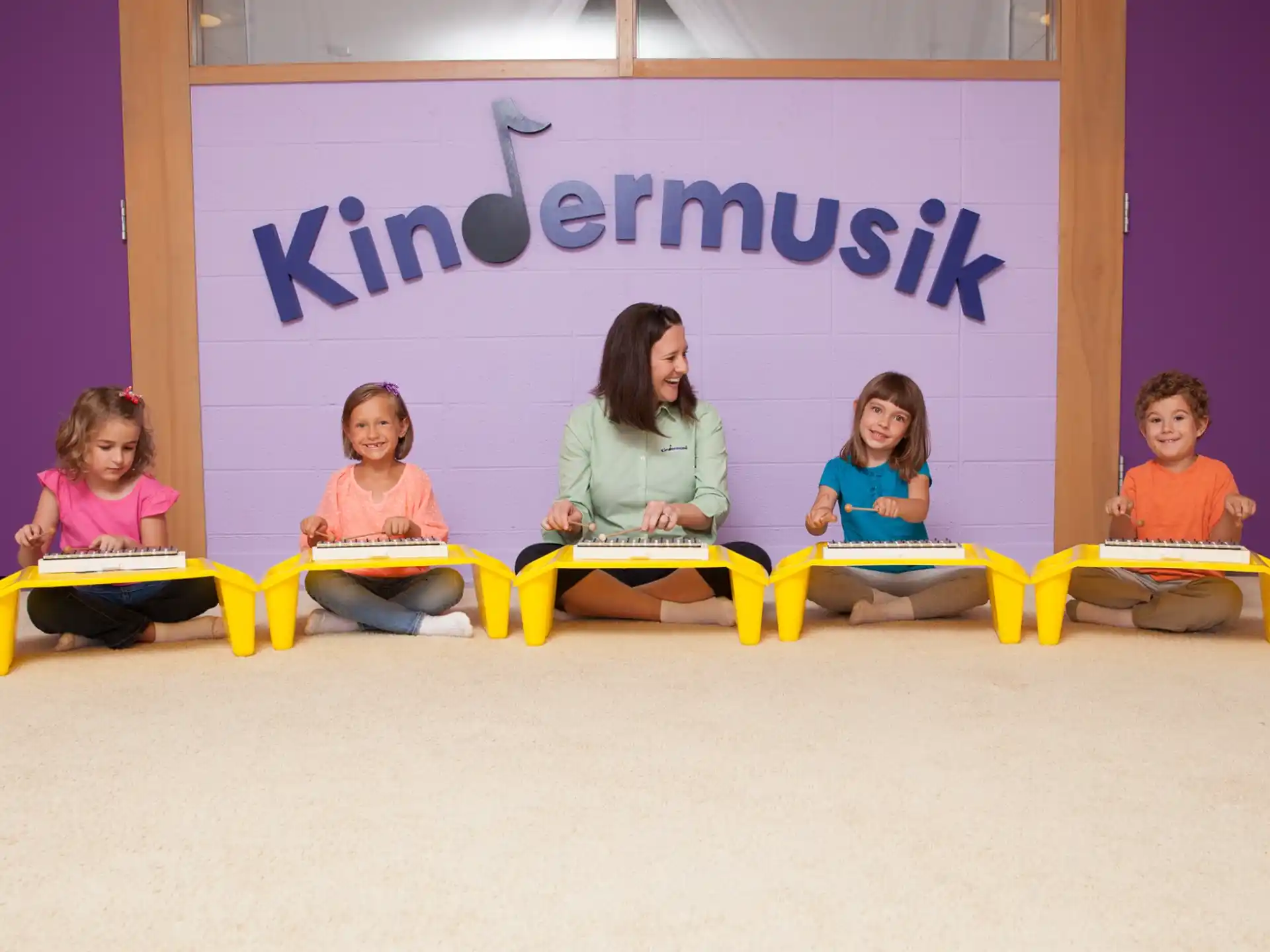 a group of children sitting on yellow chairs in front of a sign